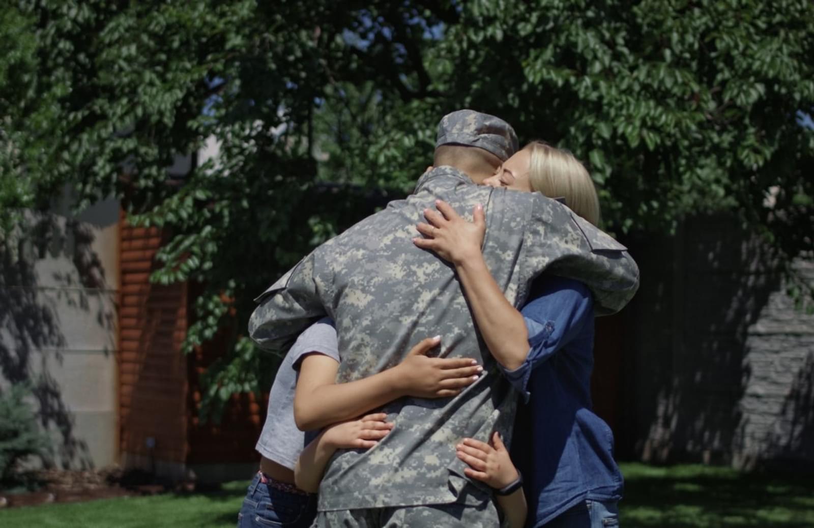 Man in military uniform hugging woman and child
