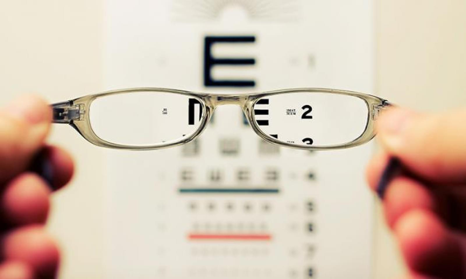 Vision chart with someone holding up glasses in foreground