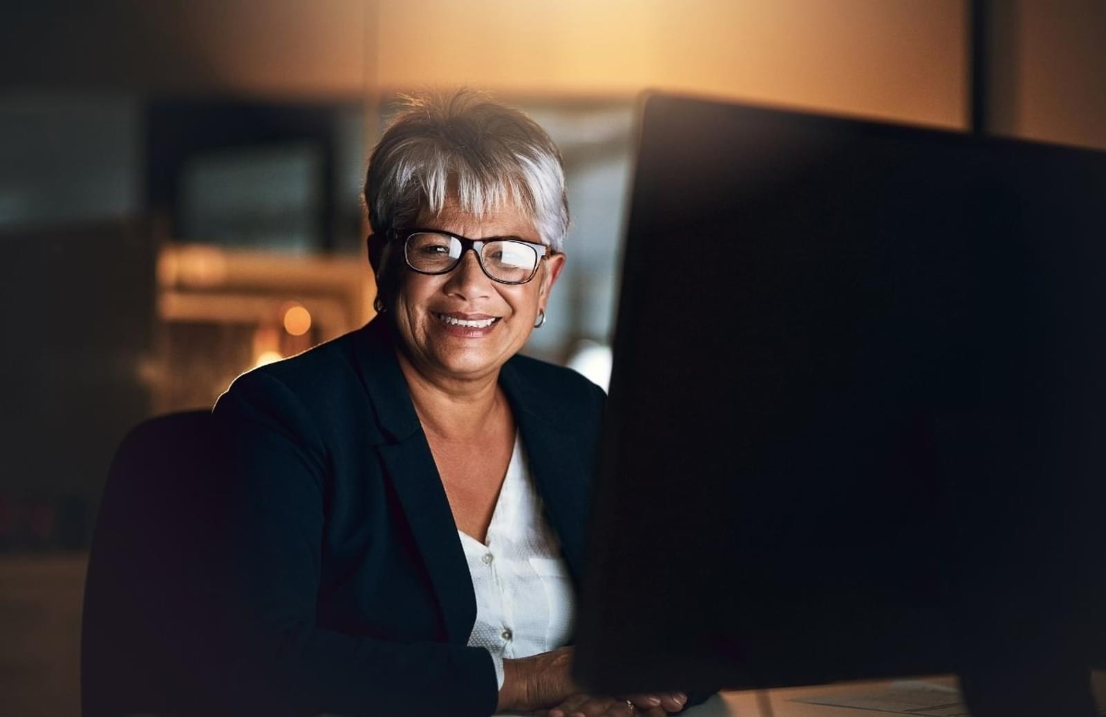 Woman sitting at desk smiling at camera while working on computer