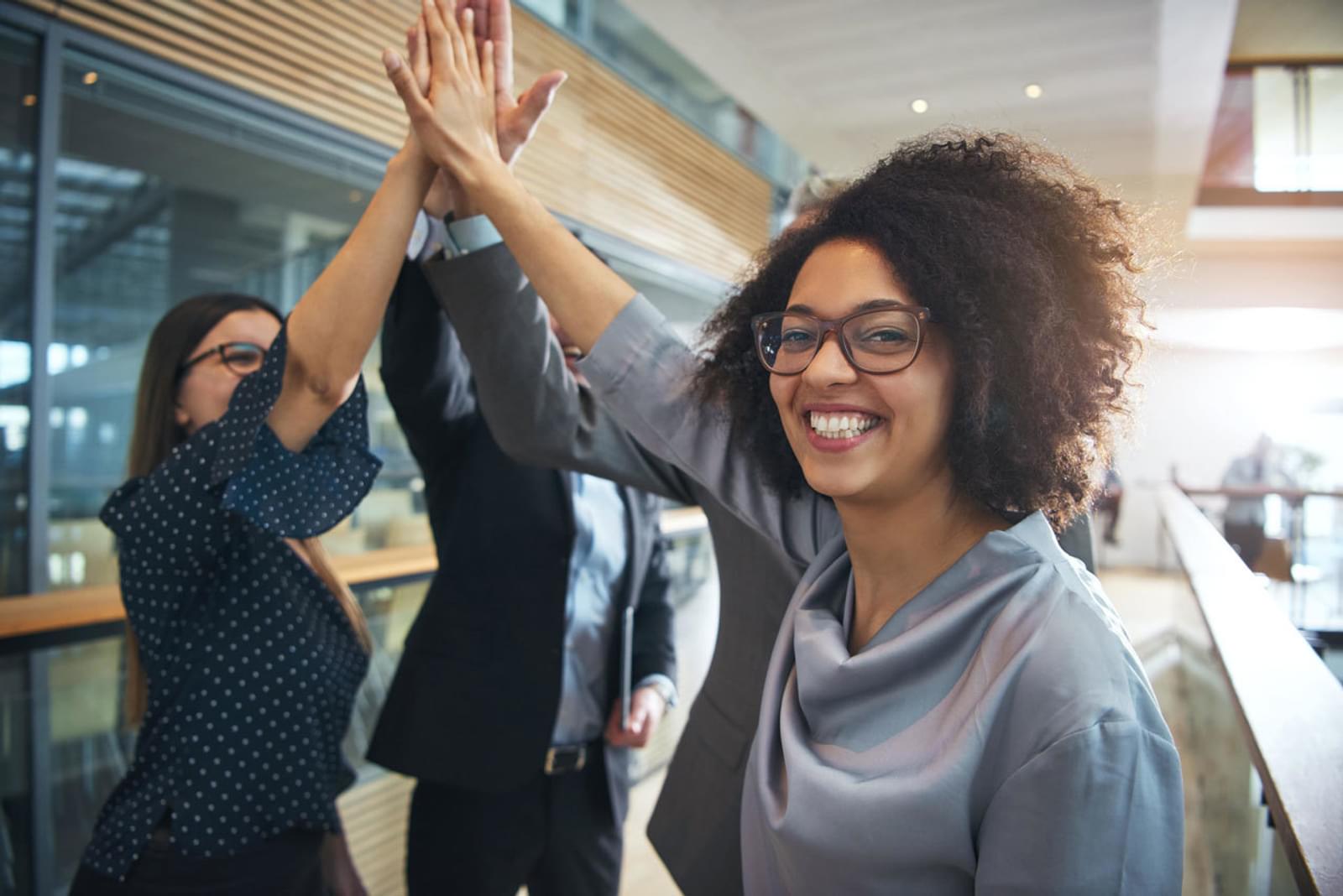Smiling black businesswoman giving high five to office team
