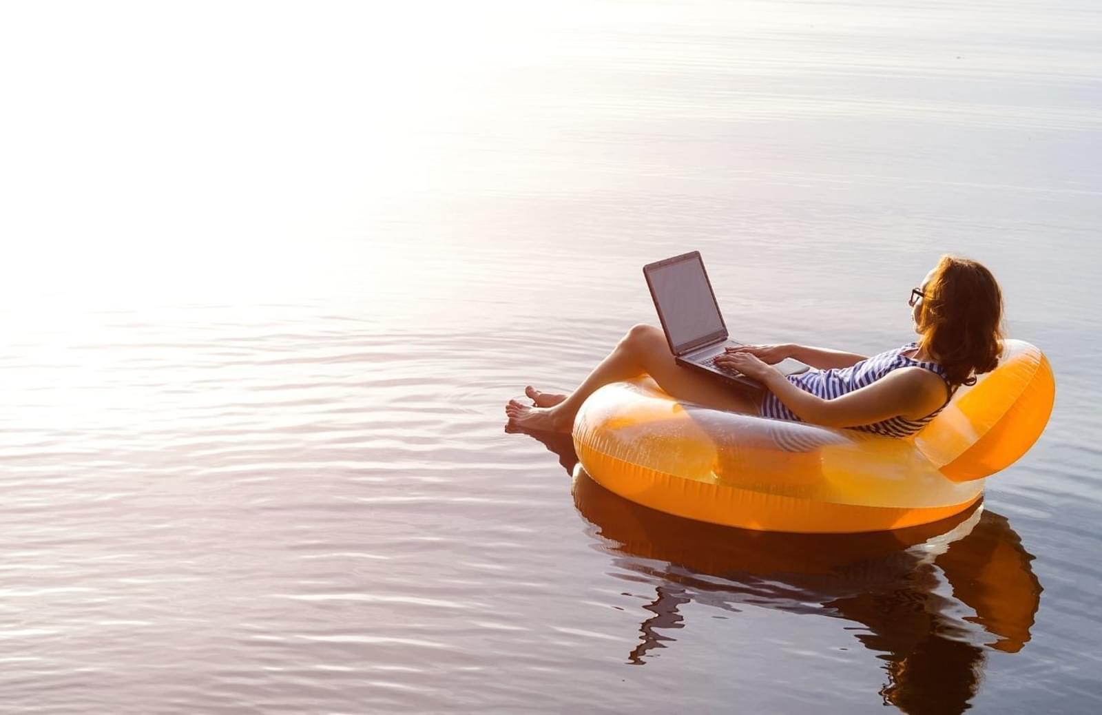 Person looking at laptop which sitting on inflatable chair floating on body of water
