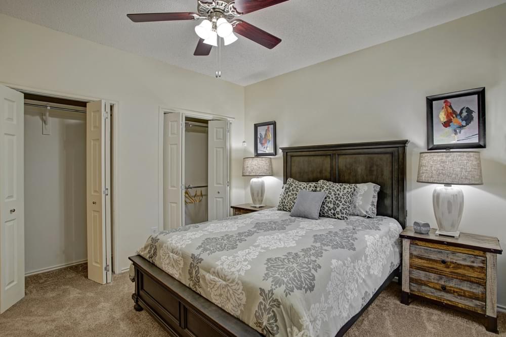 Arbors at Wolf Pen Creek Apartments modern bedroom with large bed, two nightstands, plush carpeting, ceiling fan, and spacious closets