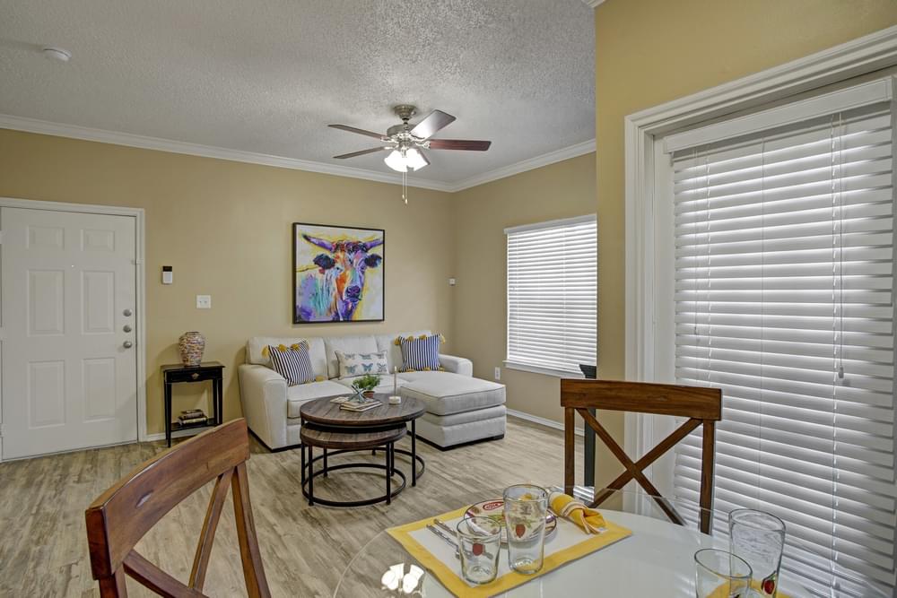 Arbors at Wolf Pen Creek Apartments Cozy living room with a sectional sofa, round tables, ceiling fan, and dining area.