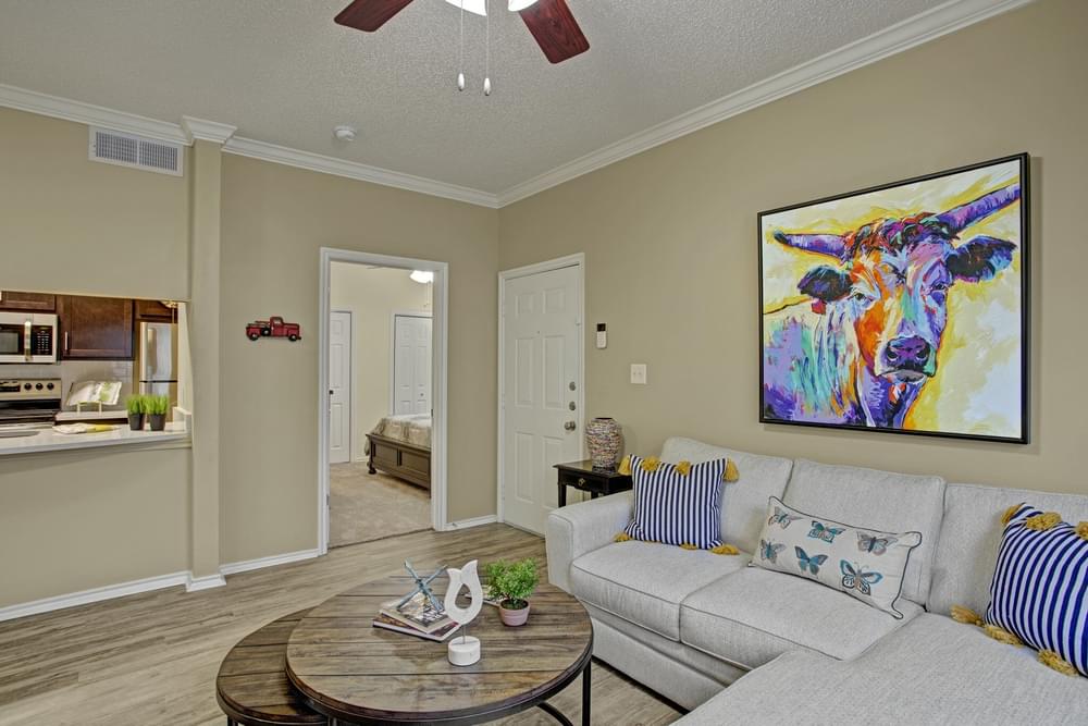 Arbors at Wolf Pen Creek Apartments Arbors at Wolf Pen Creek Apartments Cozy living room with a sectional sofa, round tables, ceiling fan, and dining area.