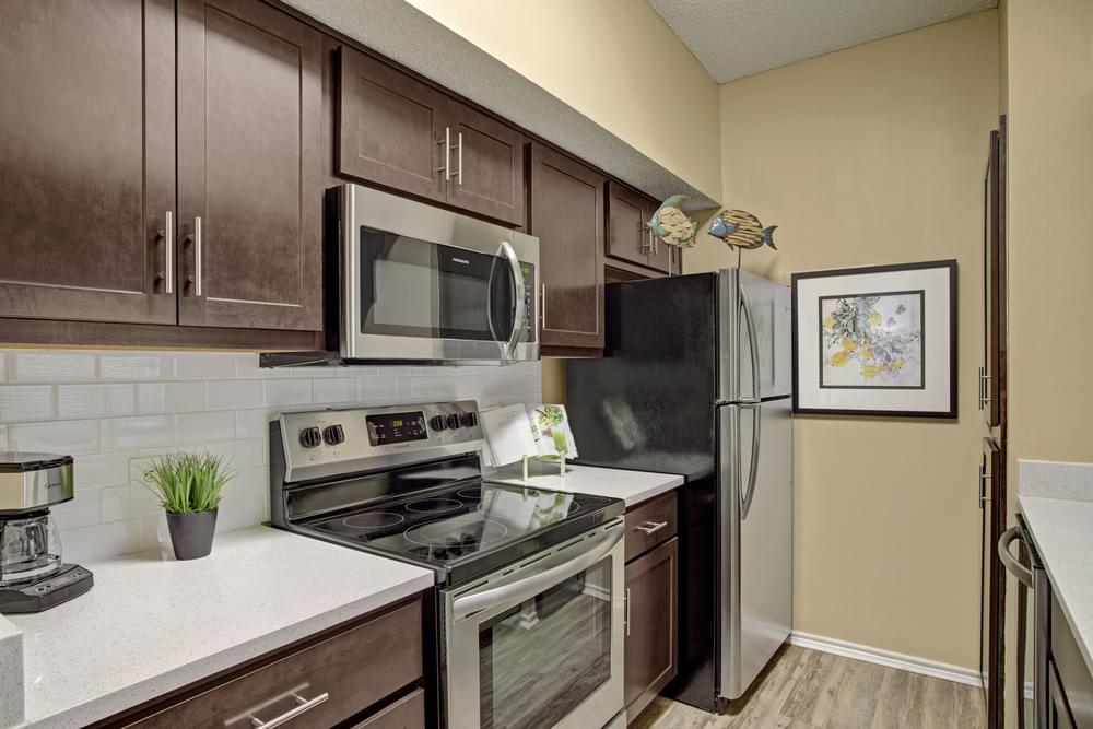 Arbors at Wolf Pen Creek Apartments Modern kitchen with dark wood cabinets, stainless steel appliances, white countertops, and decorative wall art.