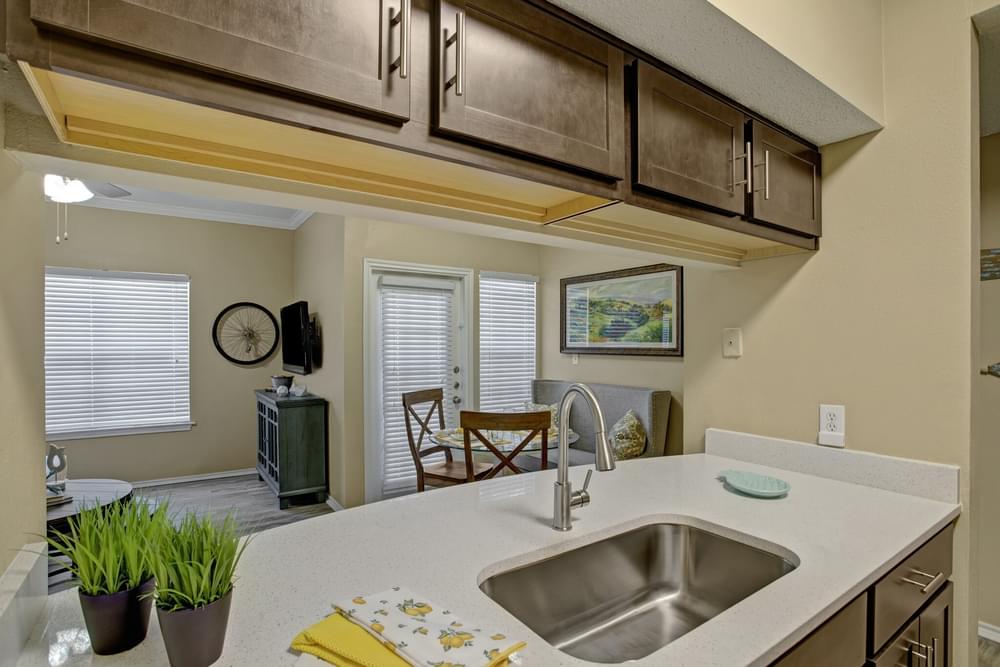 Arbors at Wolf Pen Creek Apartments Modern kitchen with dark wood cabinets, stainless steel appliances, white countertops, and decorative wall art.