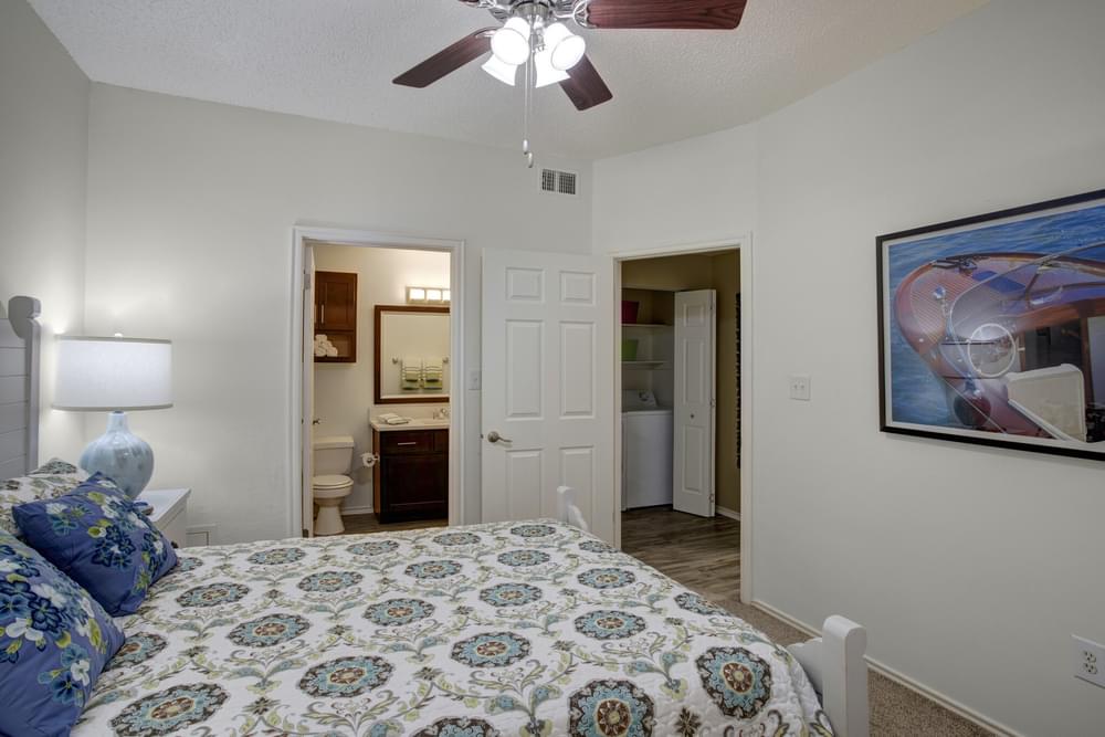 Arbors at Wolf Pen Creek Apartments whimsical bedroom with large bed, wall art, en-suite bathroom, and ceiling fan