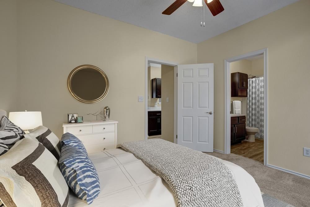 Arbors at Wolf Pen Creek Apartments large bedroom with large bed, wall art, en-suite bathroom, and ceiling fan