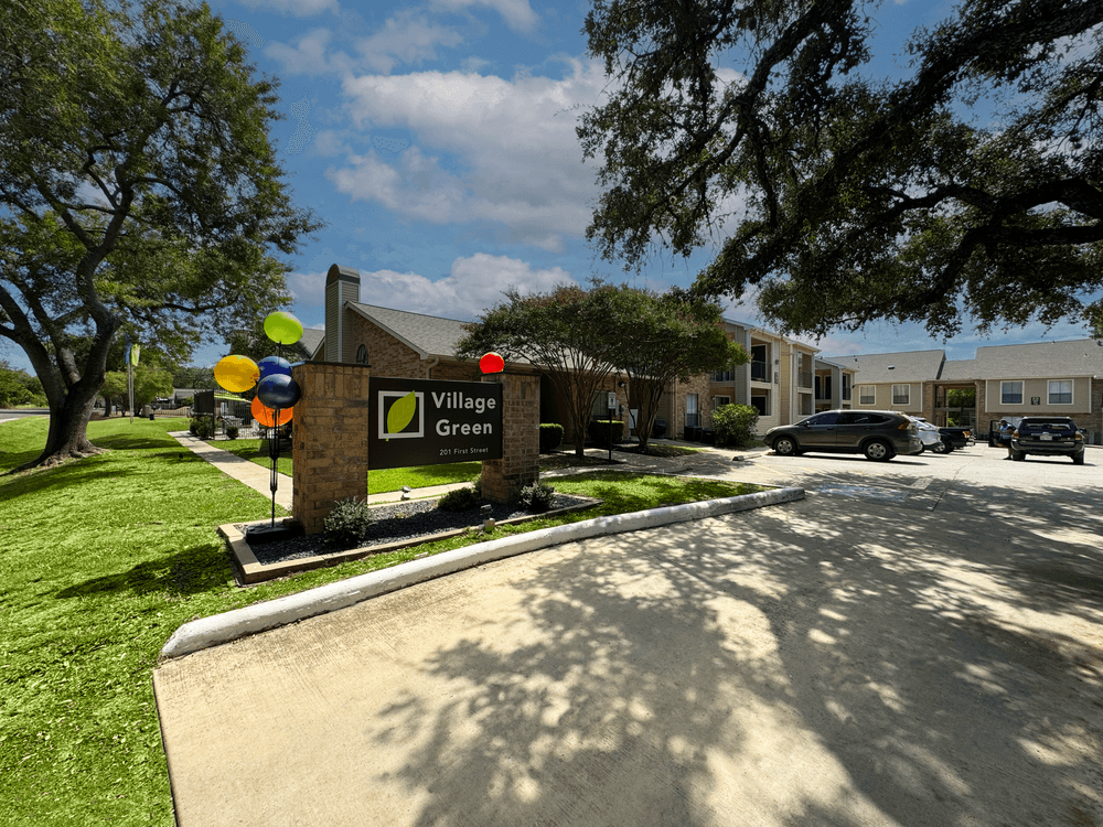 Village Green apartments large outdoor sign with beautiful landscaping, green grass, and a blue sky