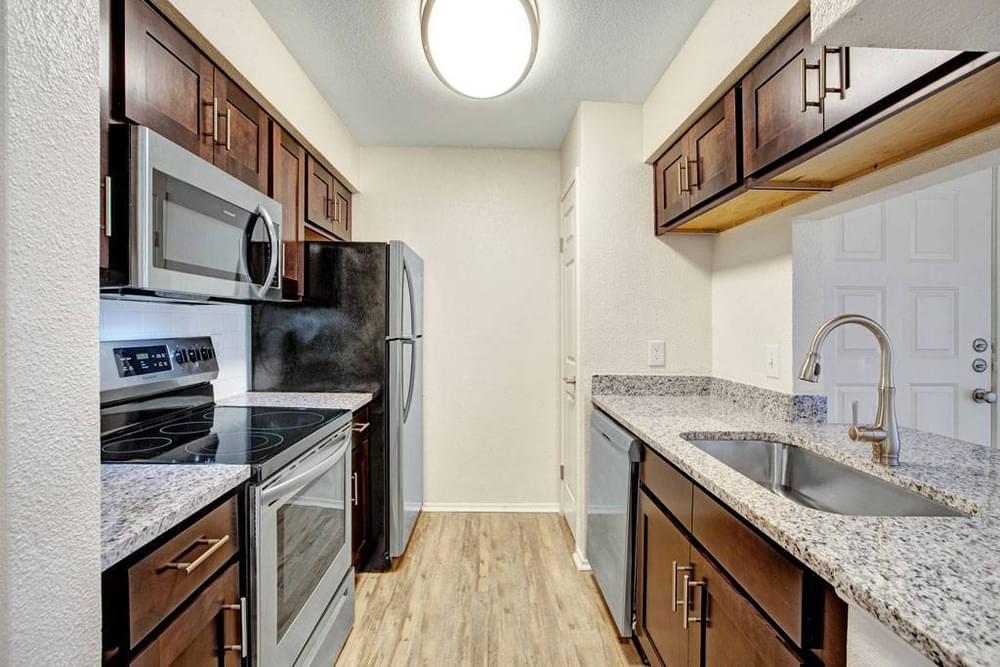 Village Green apartments Kitchen with large granite counters, wooden cabinets, dish washer, fridge and sink.
