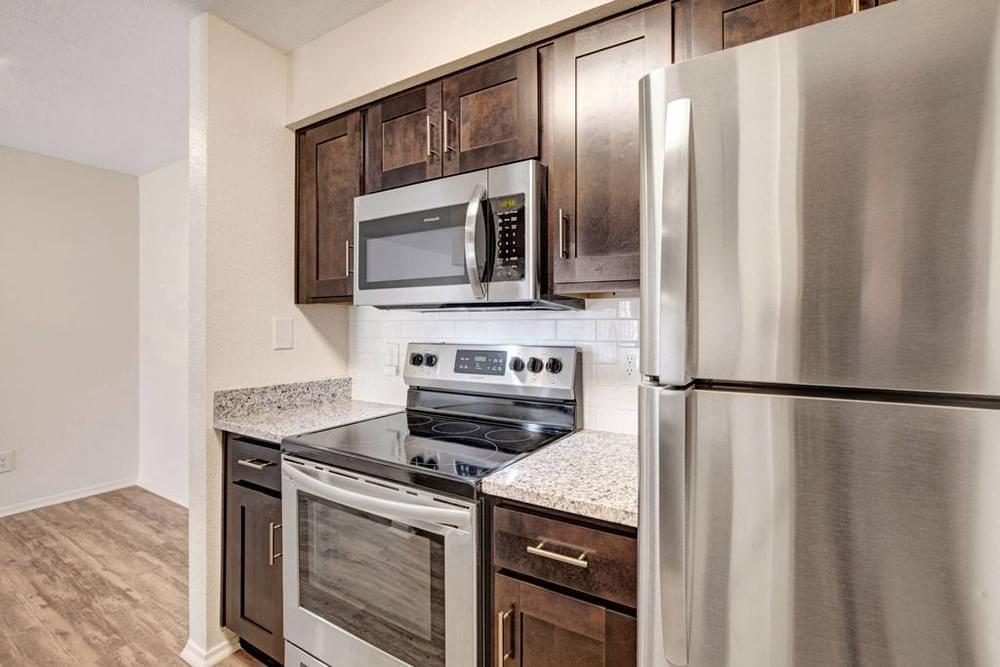 Village Green apartments Kitchen with large granite counters, wooden cabinets, stainless steel appliances, and subway tile backsplash.