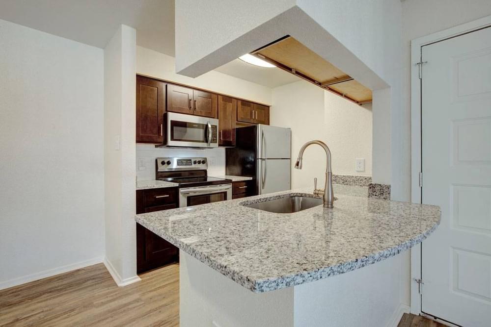 Village Green apartments Kitchen with large granite counter for cooking or bar stool seating, wooden cabinets, dish washer, and pantry.