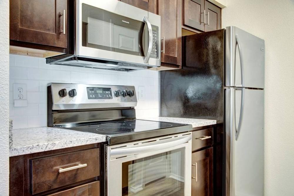 Village Green apartments Kitchen with large granite counters, wooden cabinets, stainless steel appliances, and subway tile backsplash.