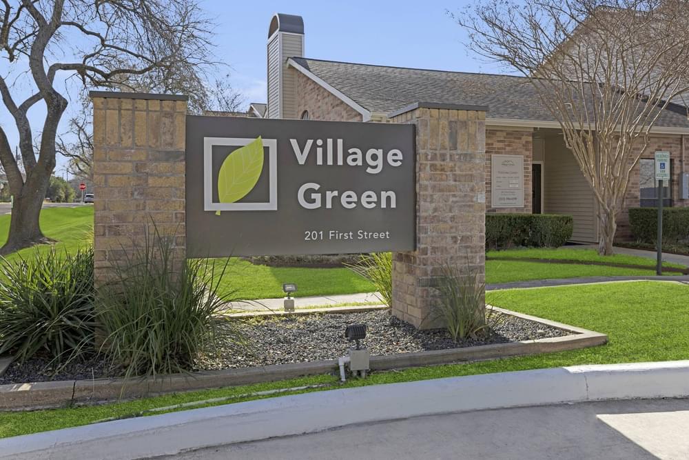 Village Green apartments large outdoor sign with beautiful landscaping, green grass, and a blue sky