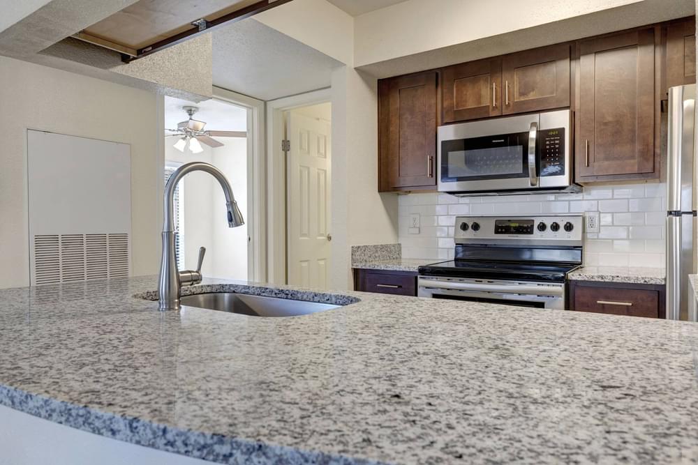 Village Green apartments Kitchen with large granite counter for cooking or bar stool seating, wooden cabinets, dish washer, and pantry.