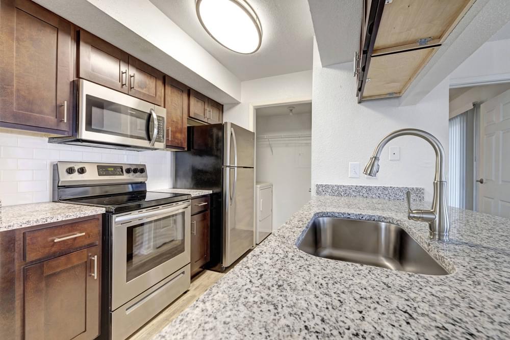 Village Green apartments Kitchen with large granite counters, wooden cabinets, stainless steel appliances, and subway tile backsplash.