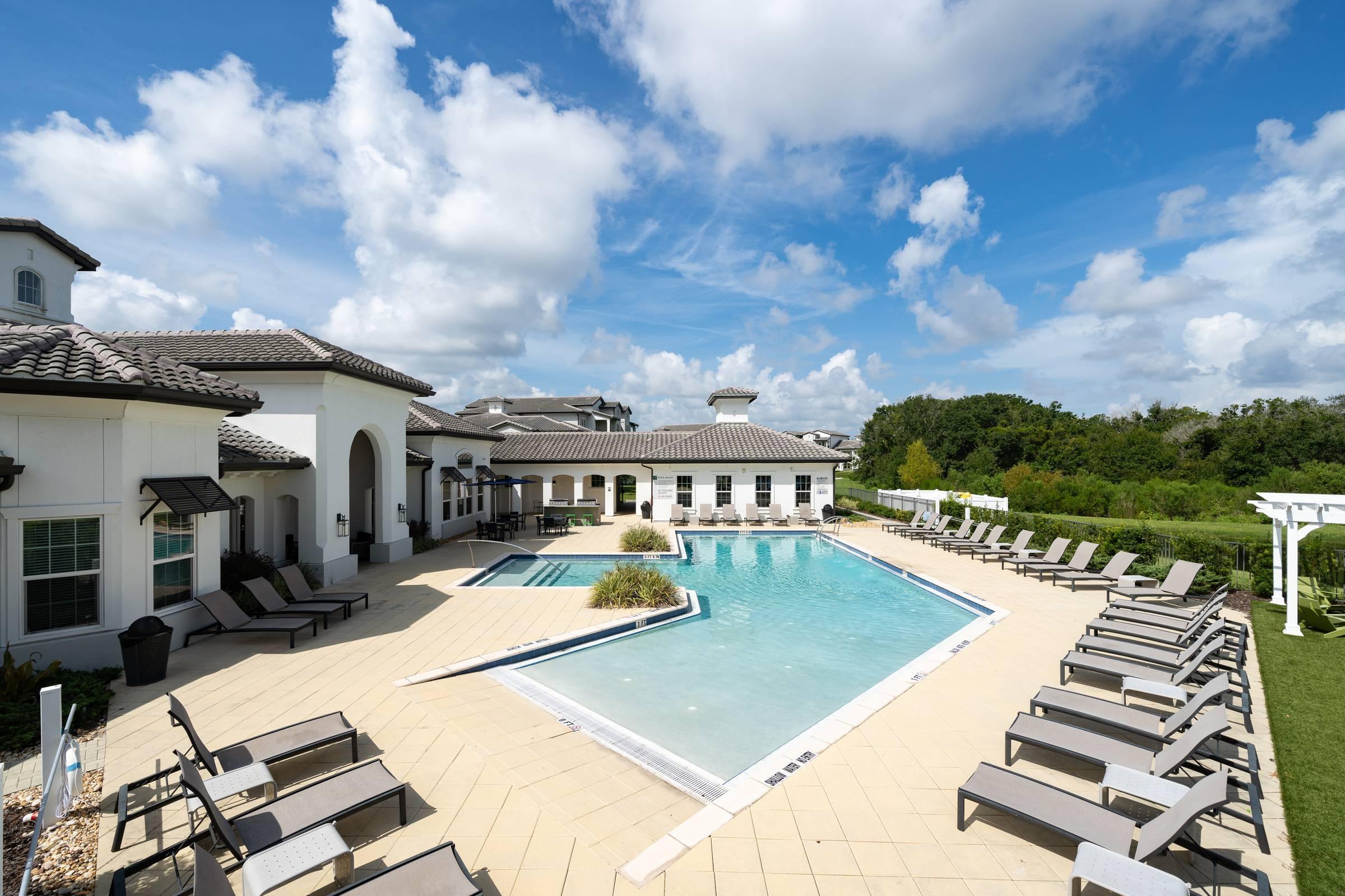 Shadetree Apartments swimming pool and sundeck with sunning lounge chairs and a gorgeous blue sky with fluffy clouds