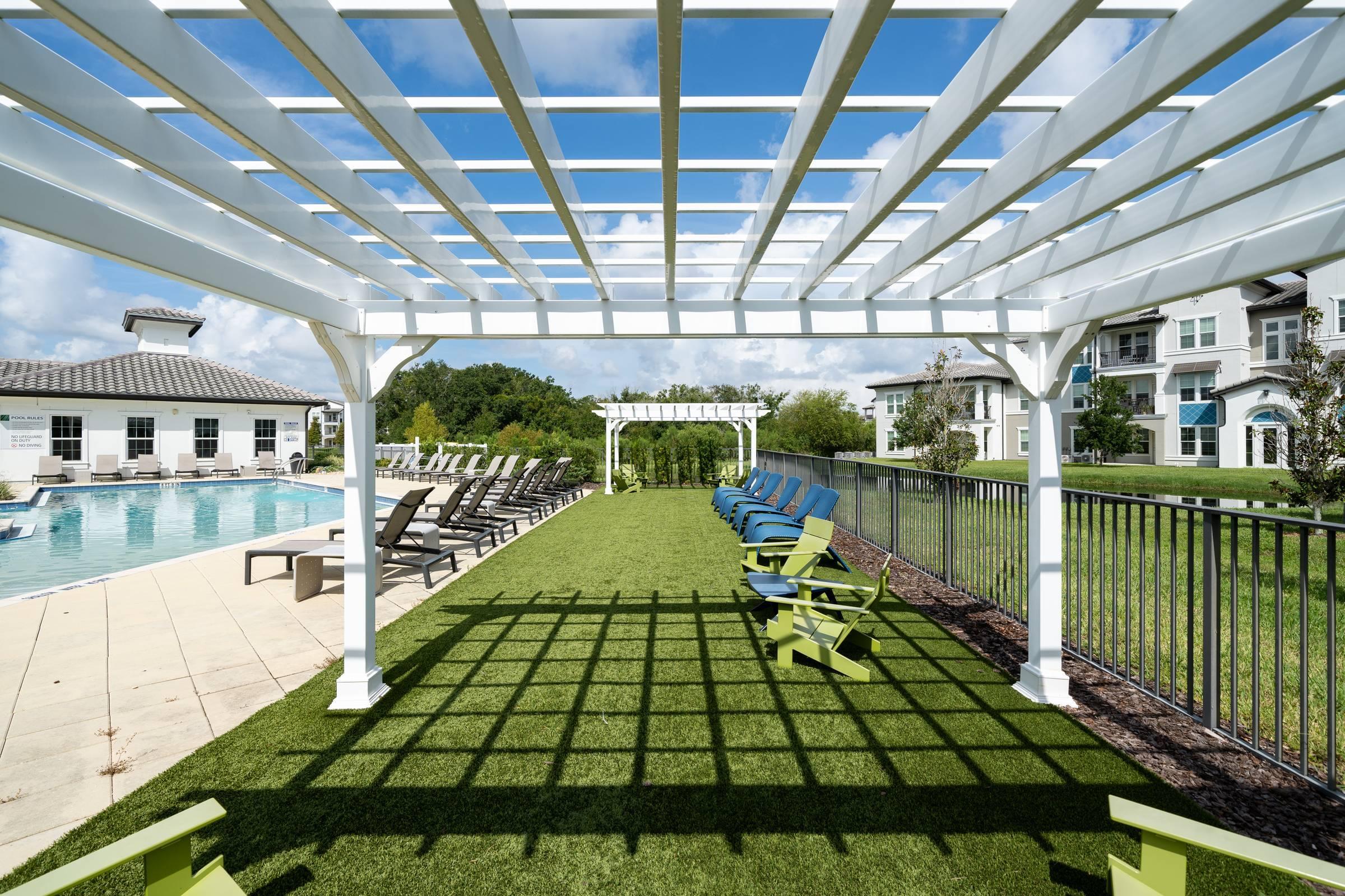 Shadetree Apartments with a large white pergola on green grass with lounge chairs