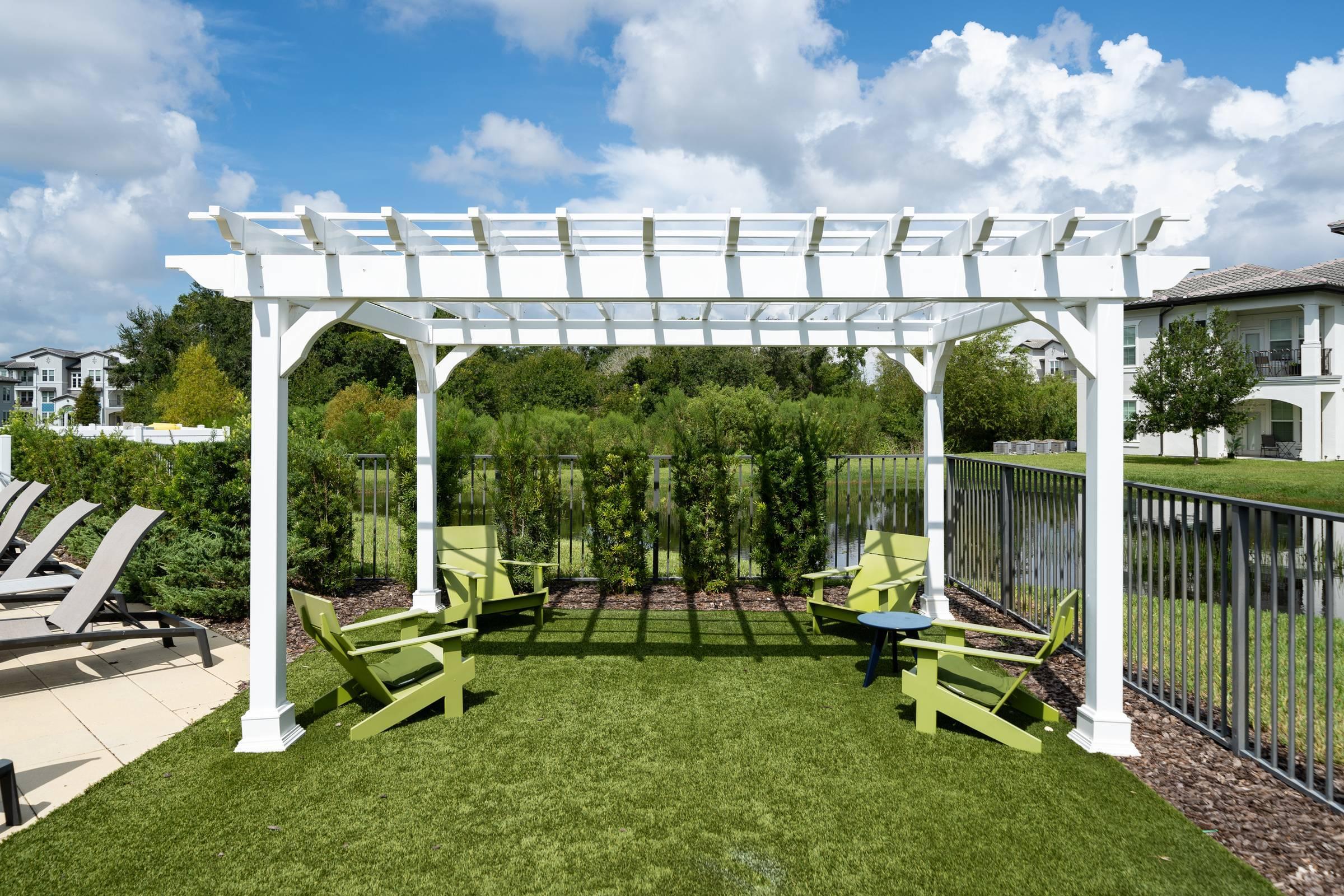 Shadetree Apartments with a large white pergola on green grass with lounge chairs