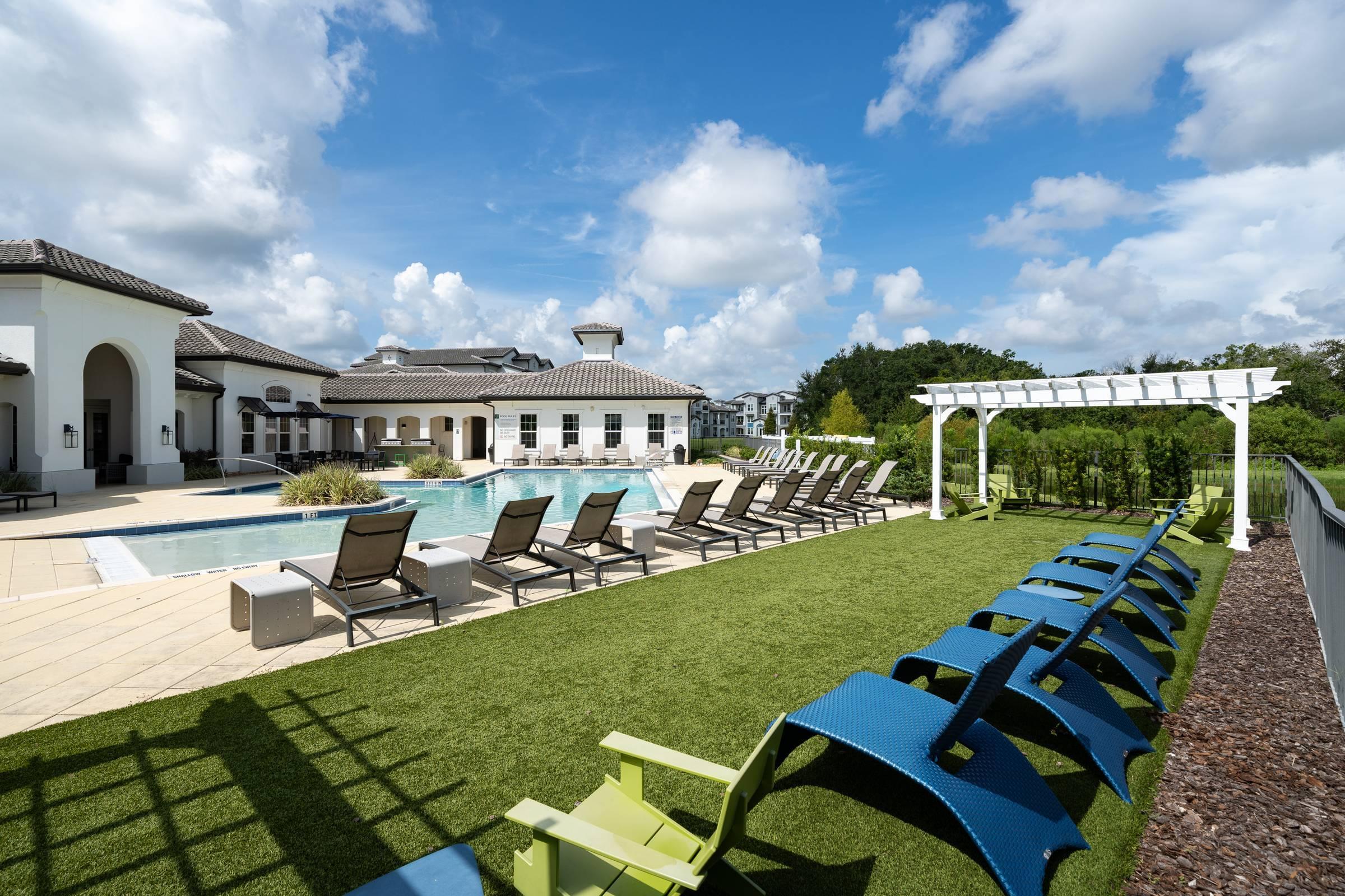 Shadetree Apartments with lounge chairs on green grass around a sparkling swimming pool