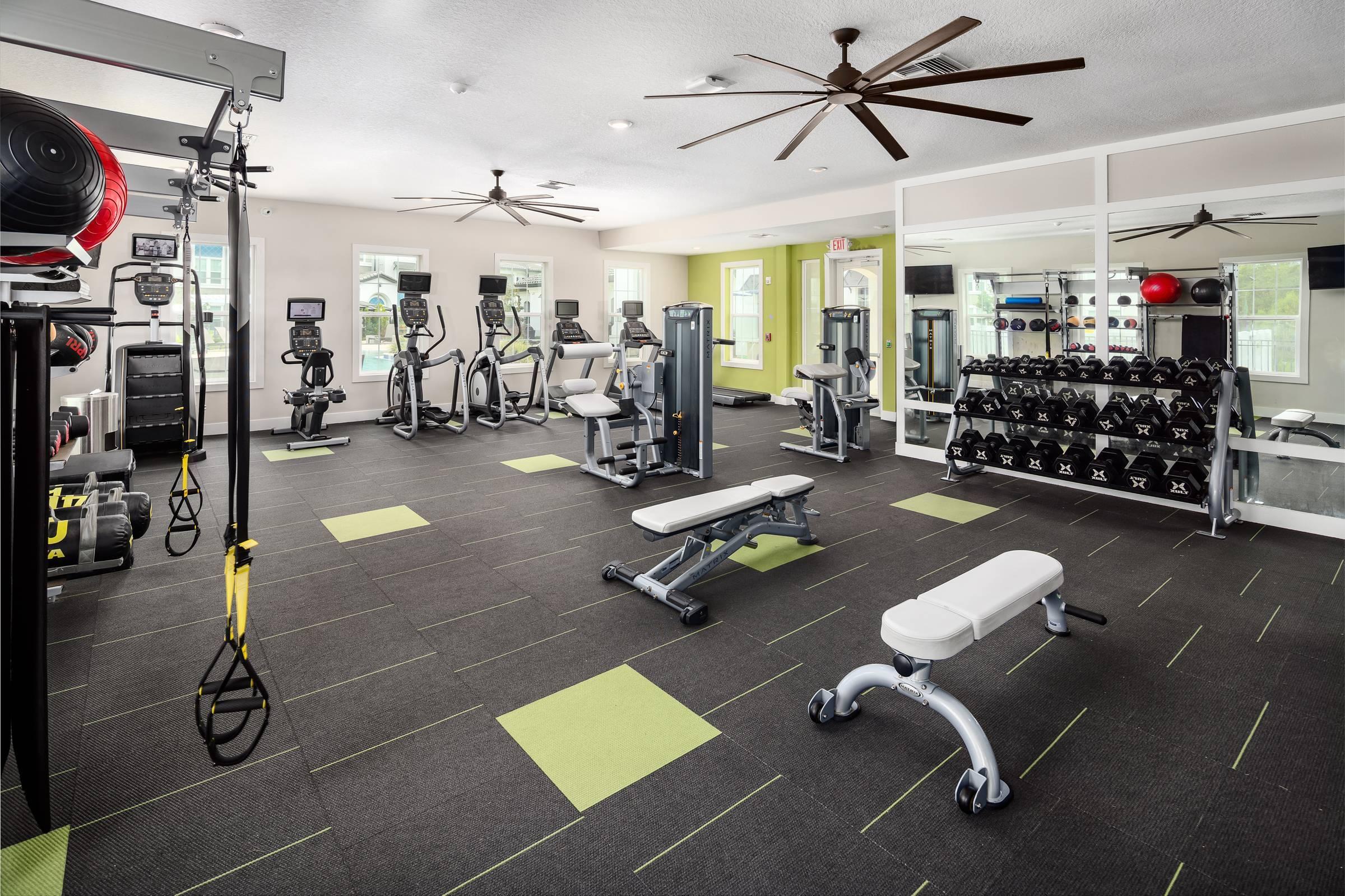 Shadetree Apartments fitness center with a large room of fitness equipment, gym flooring, and ceiling fans,