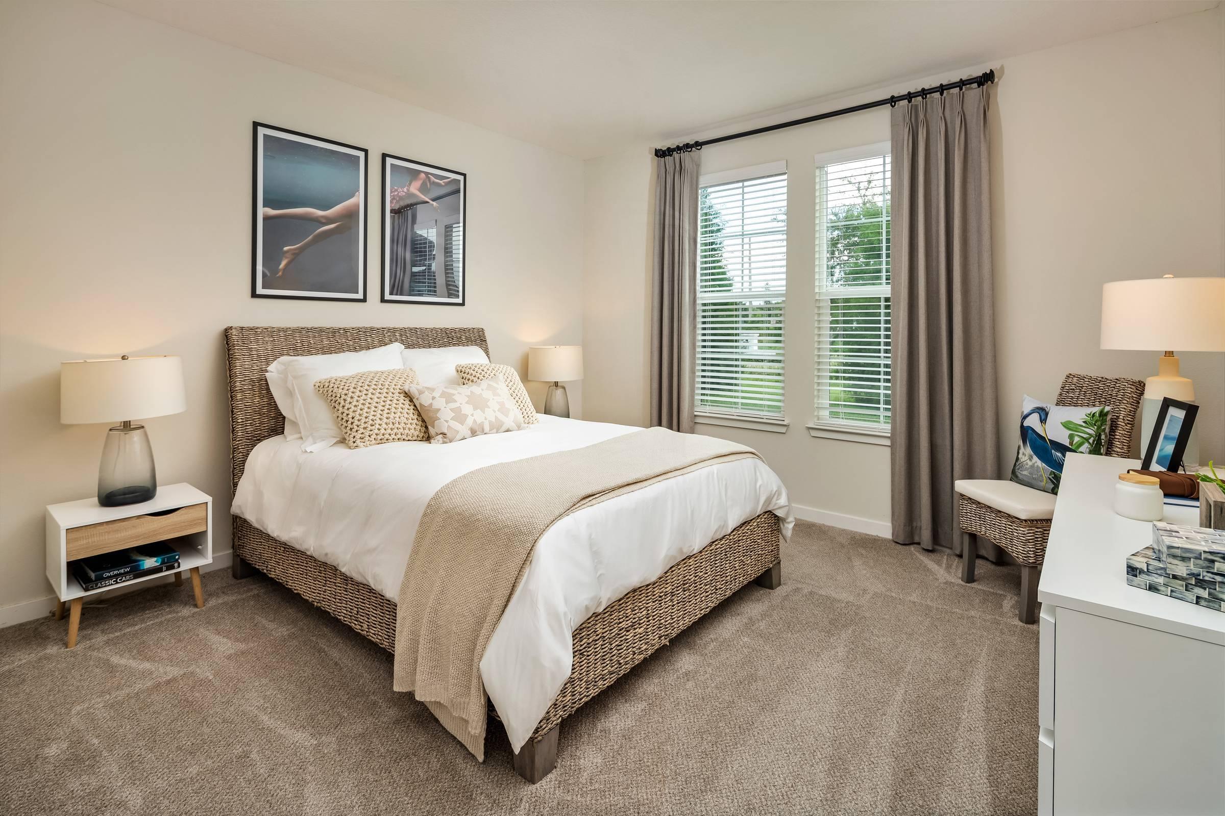 Shadetree Apartments bedroom with a large bed, throw pillows, carpet, wall art, and a large window with curtains