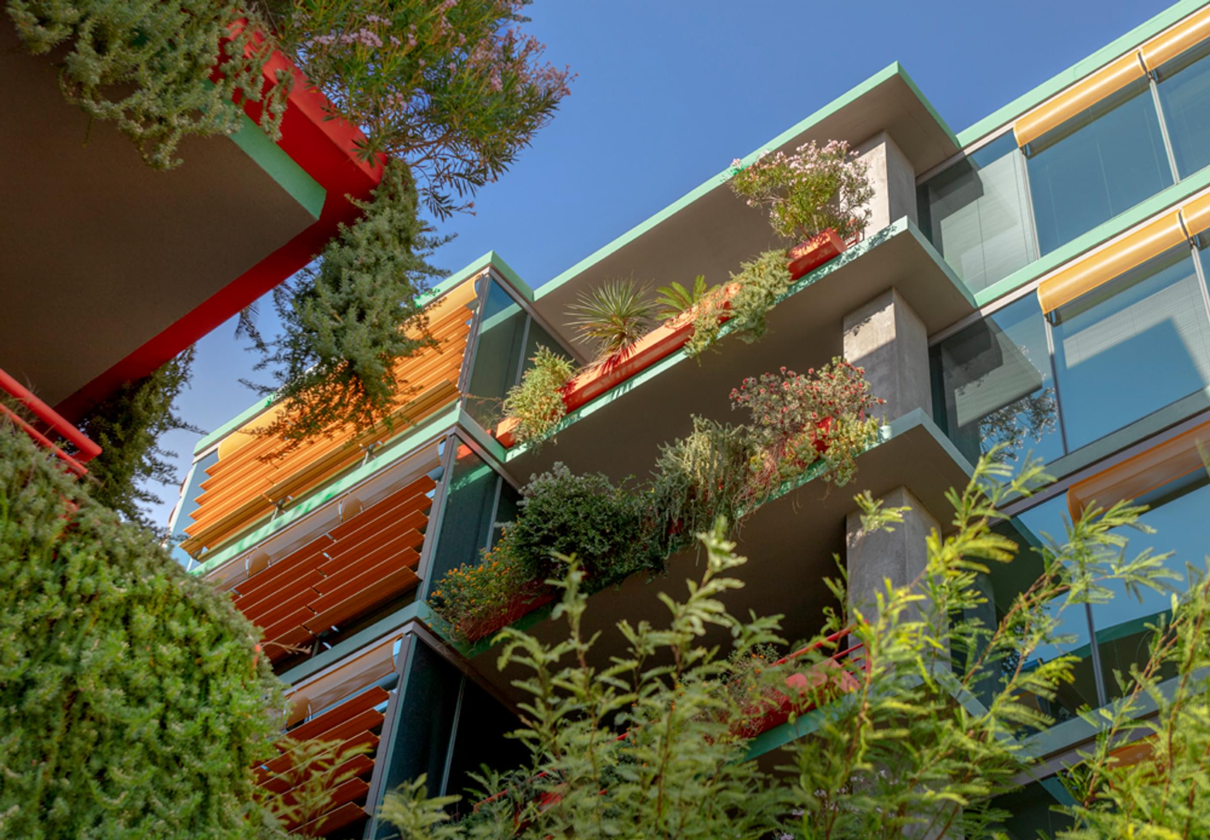 Optima Sonoran Village apartments modern building with balconies covered in lush greenery and plants, set against a clear blue sky.