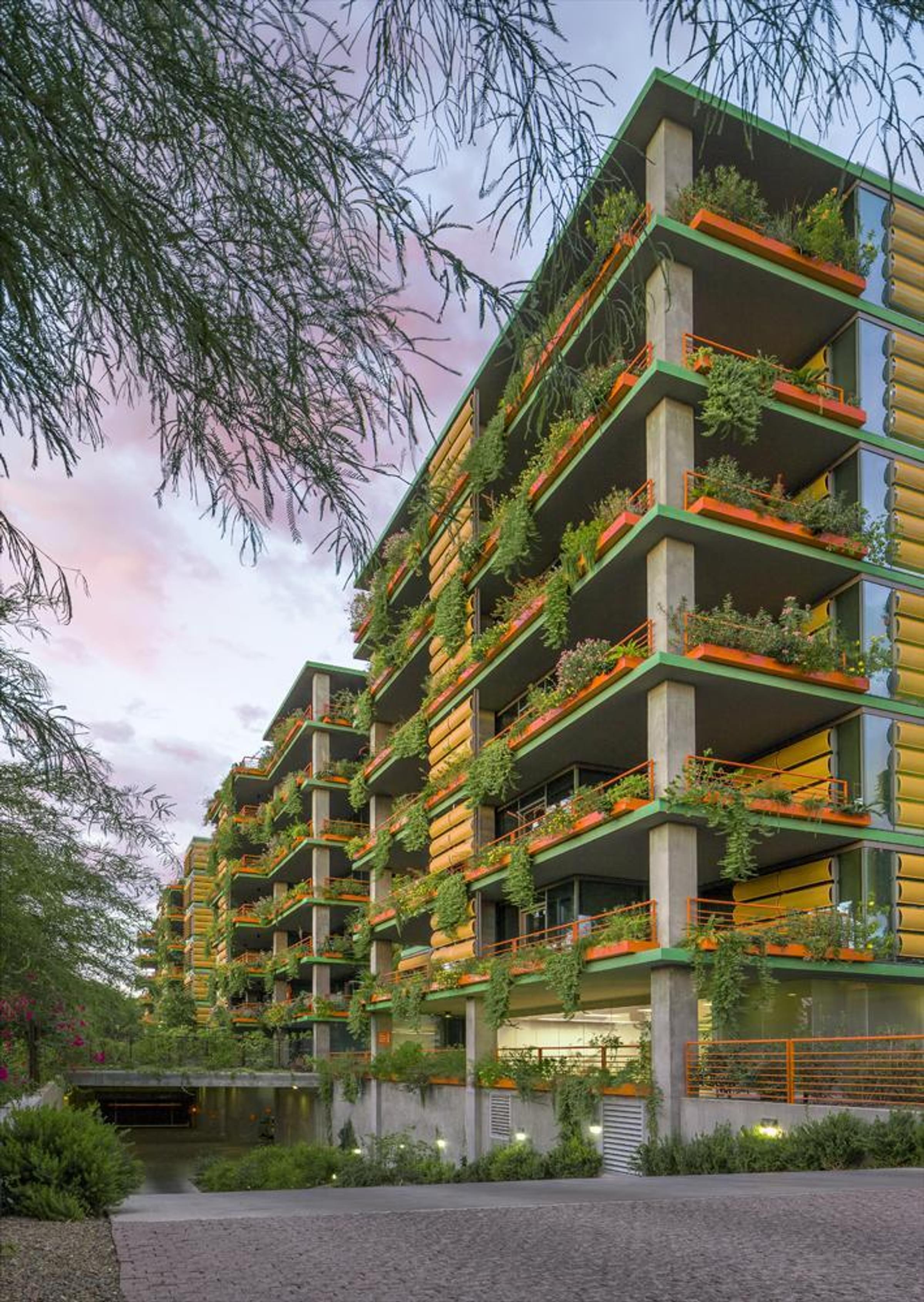 Optima Sonoran Village modern apartment building with colorful accents and lush plants on balconies, under a clear blue sky.