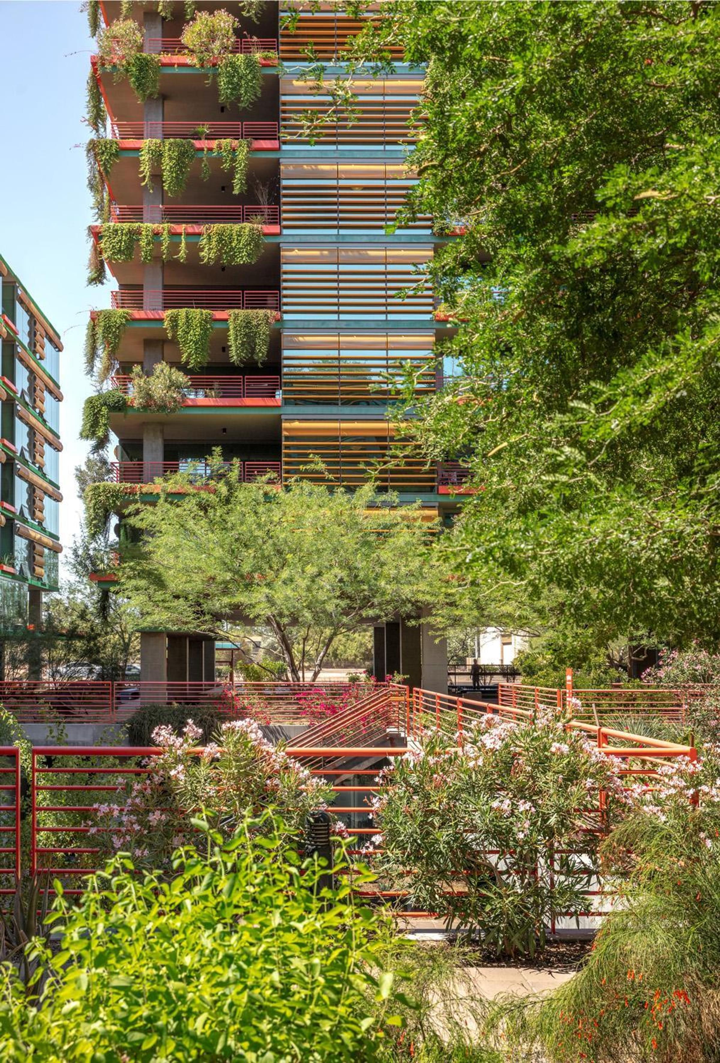 Optima Sonoran Village modern building with large glass facade framed by trees and patios, featuring outdoor seating areas below.