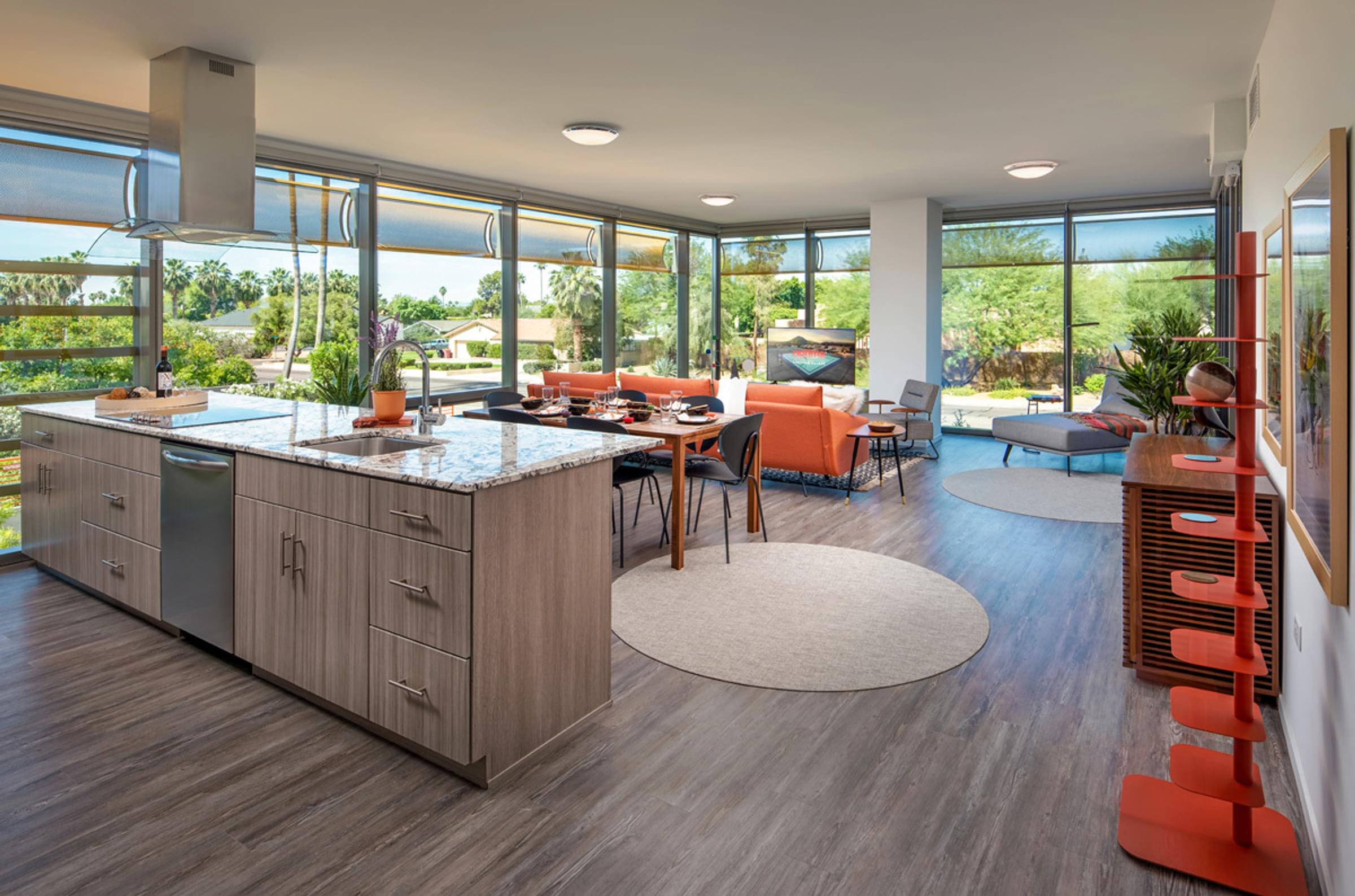 Optima Sonoran Village apartments Modern open-plan living room with large windows, orange sofa, round dining table, and a kitchen island with marble top.