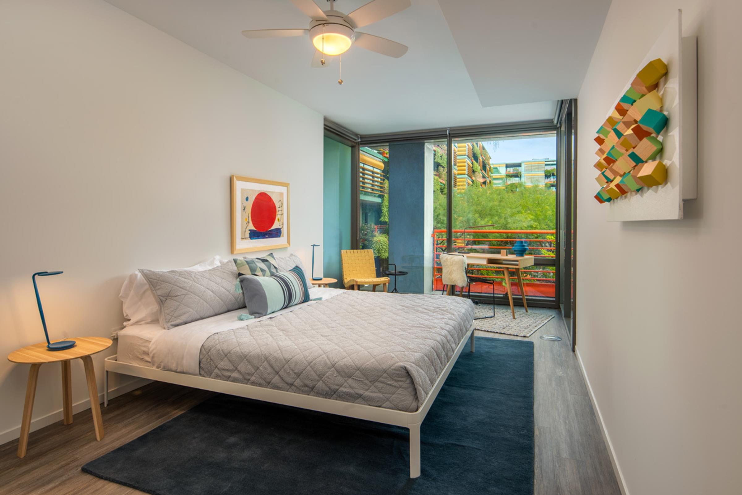 Optima Sonoran Village apartments Modern bedroom with a double bed, abstract art, indoor plants, and a balcony view through glass doors.