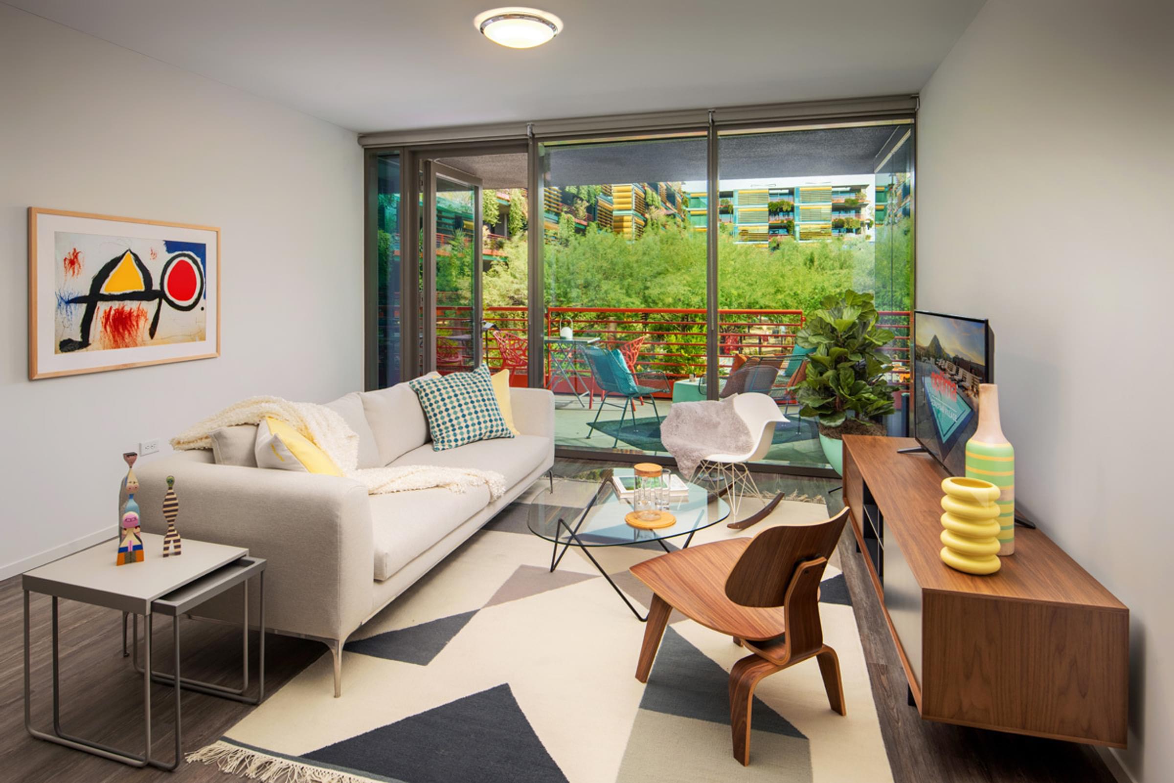 Optima Sonoran Village apartments Modern living room with a beige sofa, geometric rug, abstract art, plants, and balcony view.