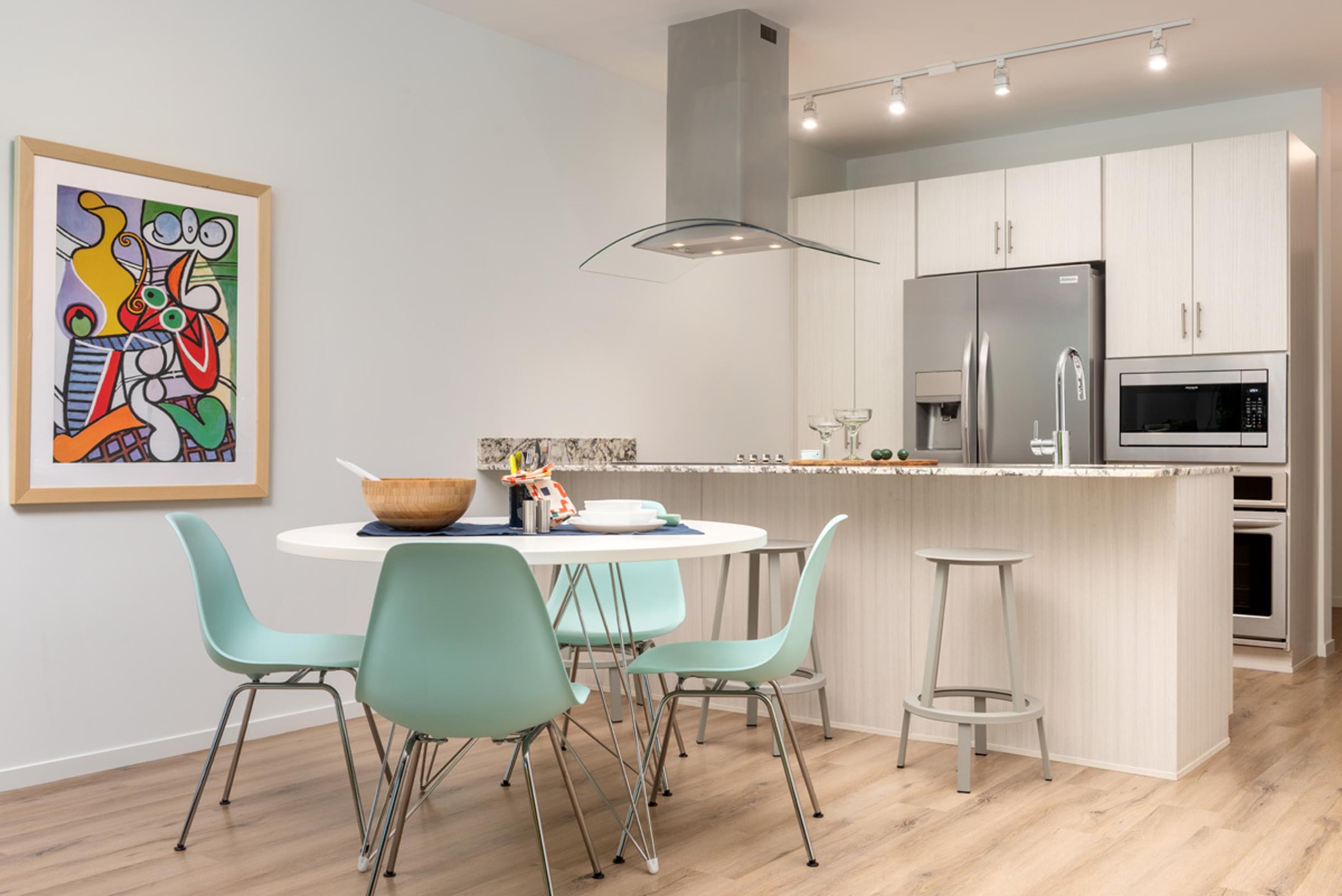Optima Sonoran Village apartments Modern kitchen with island, light wood flooring, abstract art, and pastel green chairs around a round table.