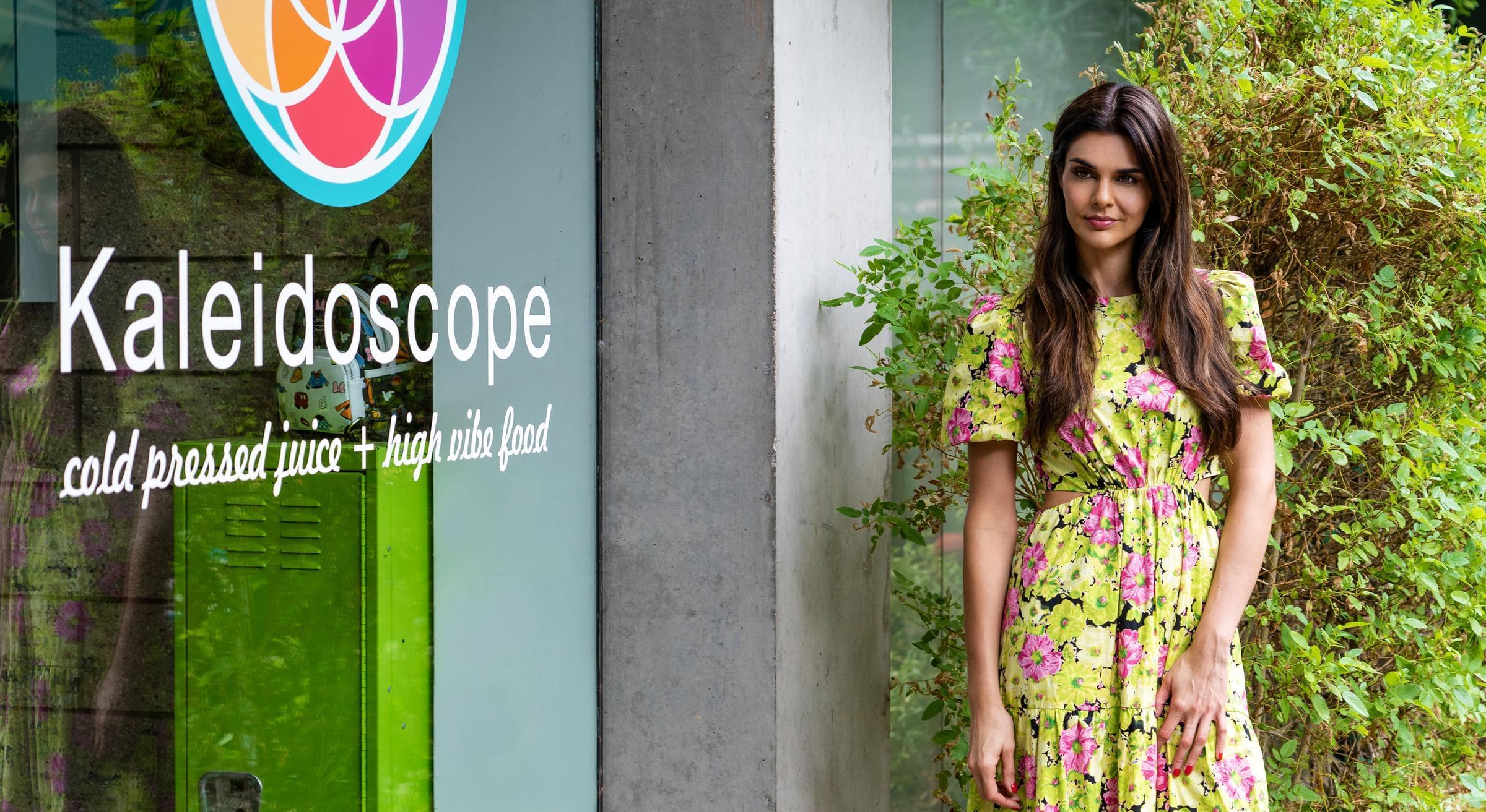Optima Sonoran Village apartments Woman in a floral dress stands outside a shop with a colorful sign that reads "Kaleidoscope".