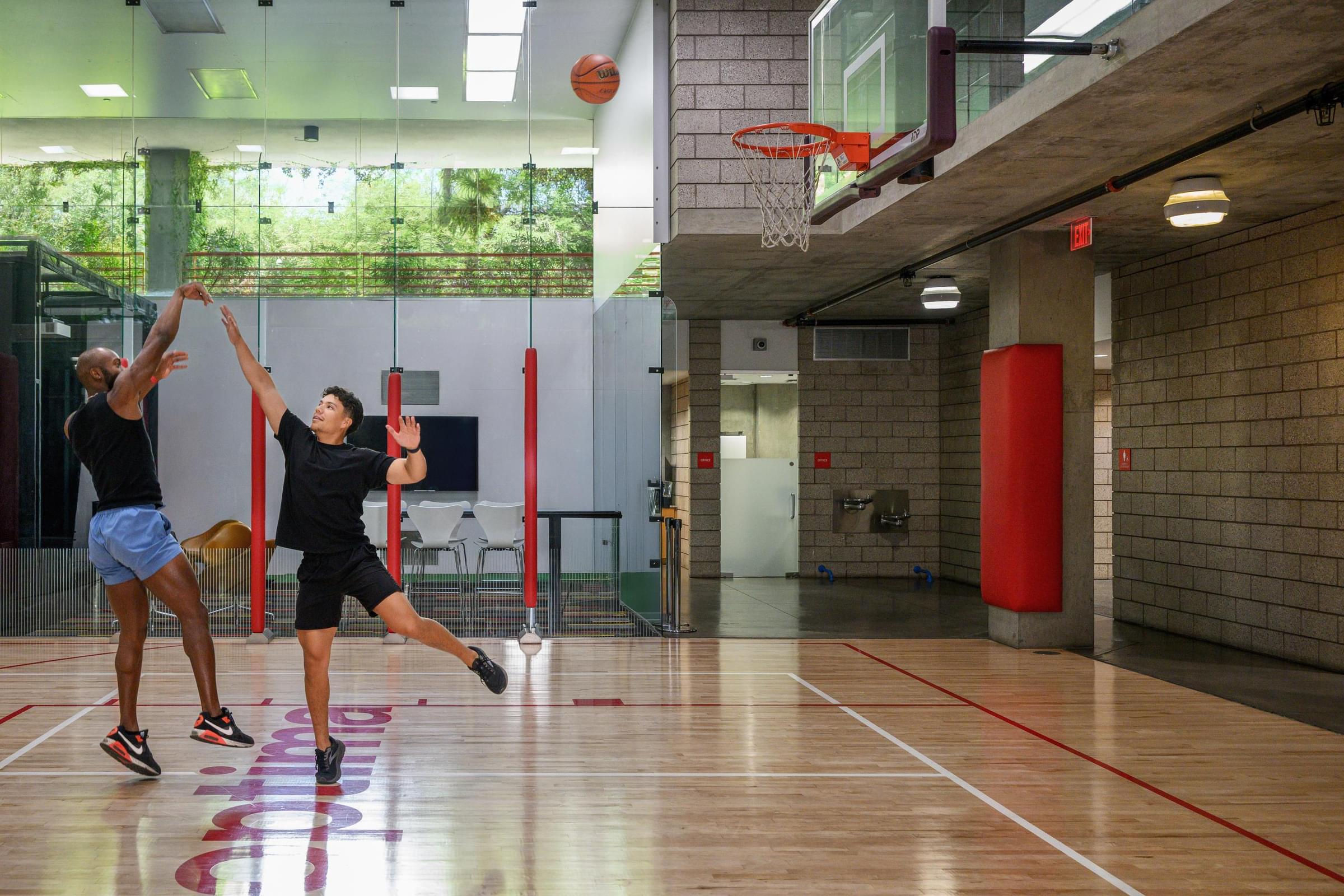 Optima Sonoran Village apartments two people playing basketball indoors; one shooting while the other attempts to block the shot.