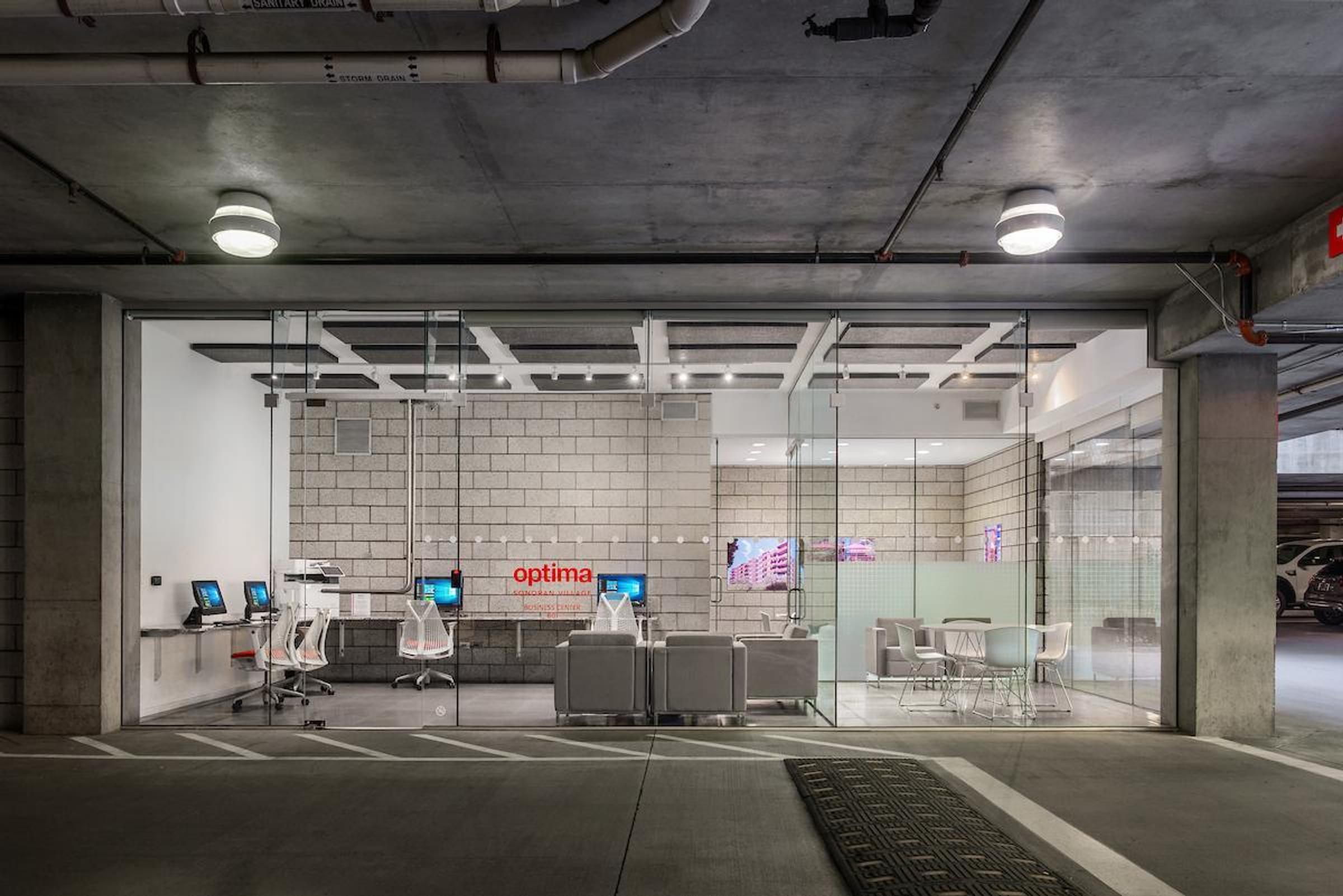 Optima Sonoran Village apartments modern office with glass walls and computers, located inside a concrete parking garage.