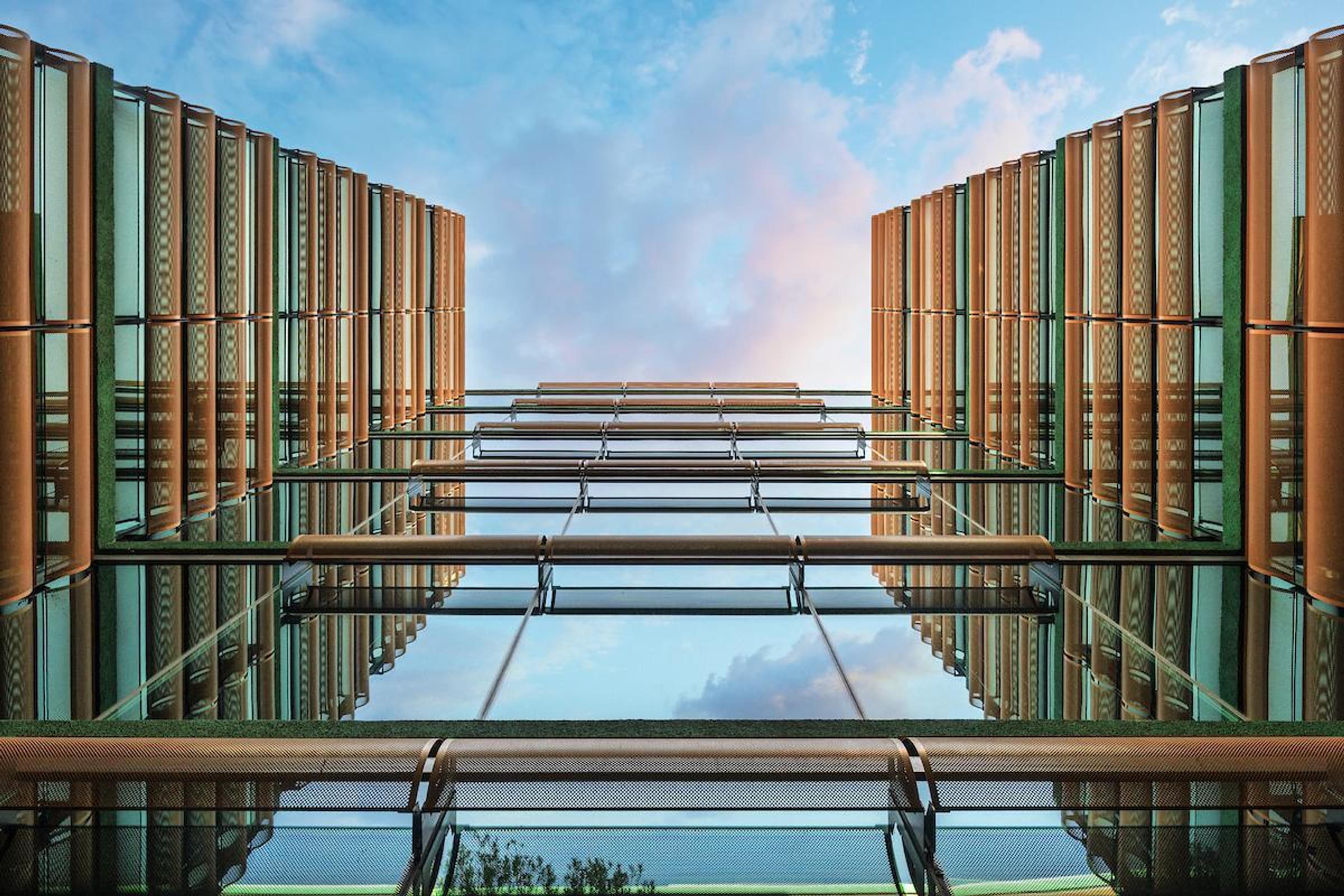 Optima Sonoran Village apartments low-angle view of a modern glass building with gold accents and a blue sky with clouds above.