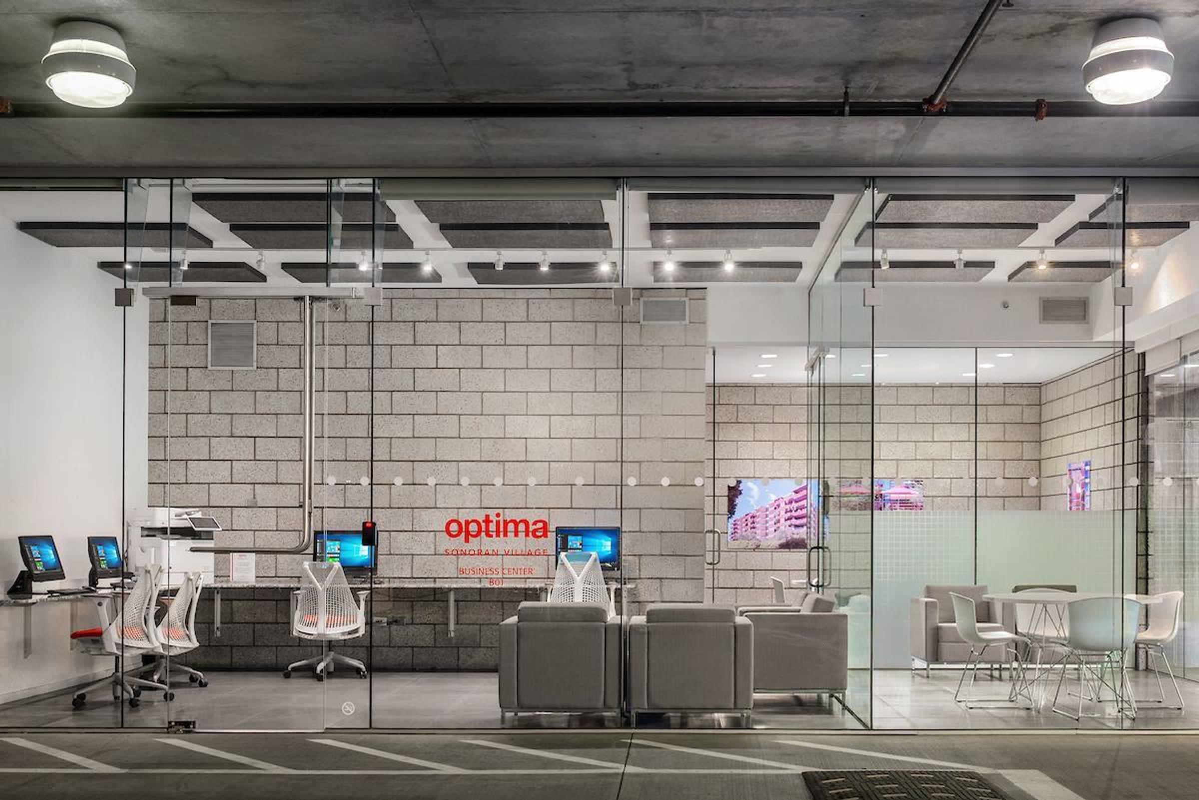 Optima Sonoran Village apartments modern office with glass walls, gray sofas, workstations with computers, and a small meeting area with chairs.