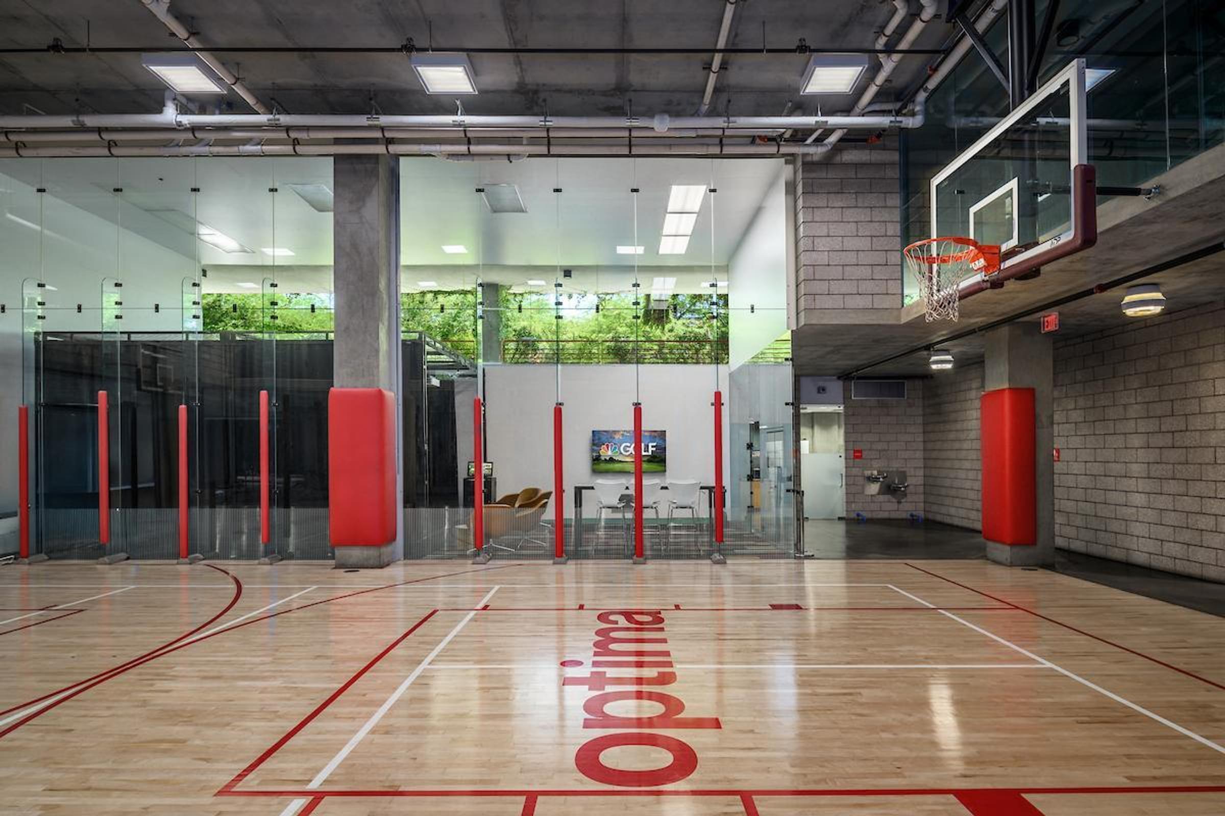 Optima Sonoran Village apartments indoor basketball court with glass walls, red accents, and a TV in a modern gym setting.