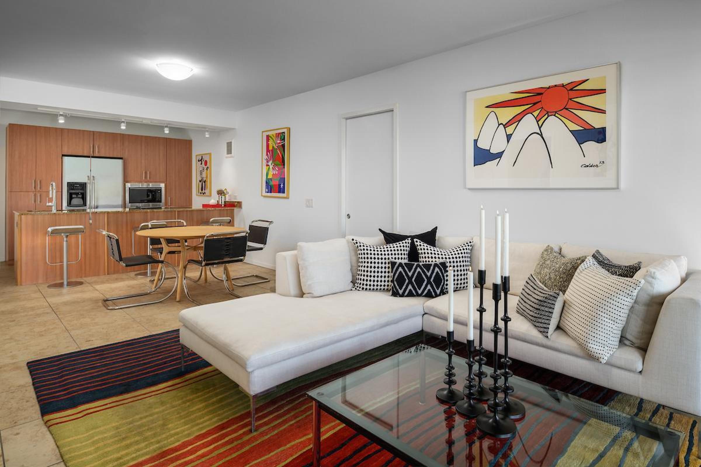 Optima Sonoran Village apartments modern living room with white sectional sofa, glass coffee table, colorful rugs, and open kitchen in background.
