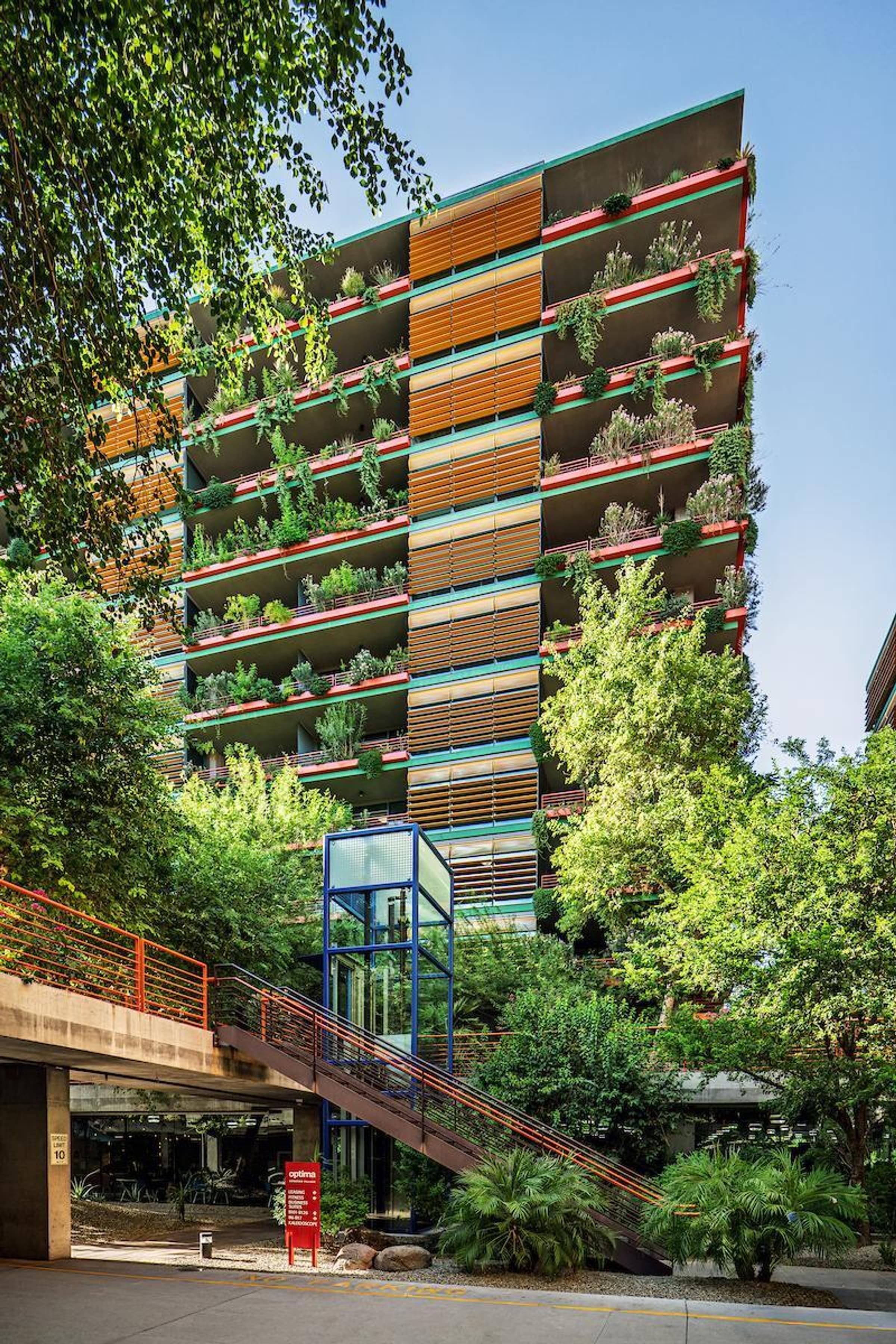 Optima Sonoran Village apartments a tall building with colorful balconies and abundant plants, surrounded by trees and greenery.