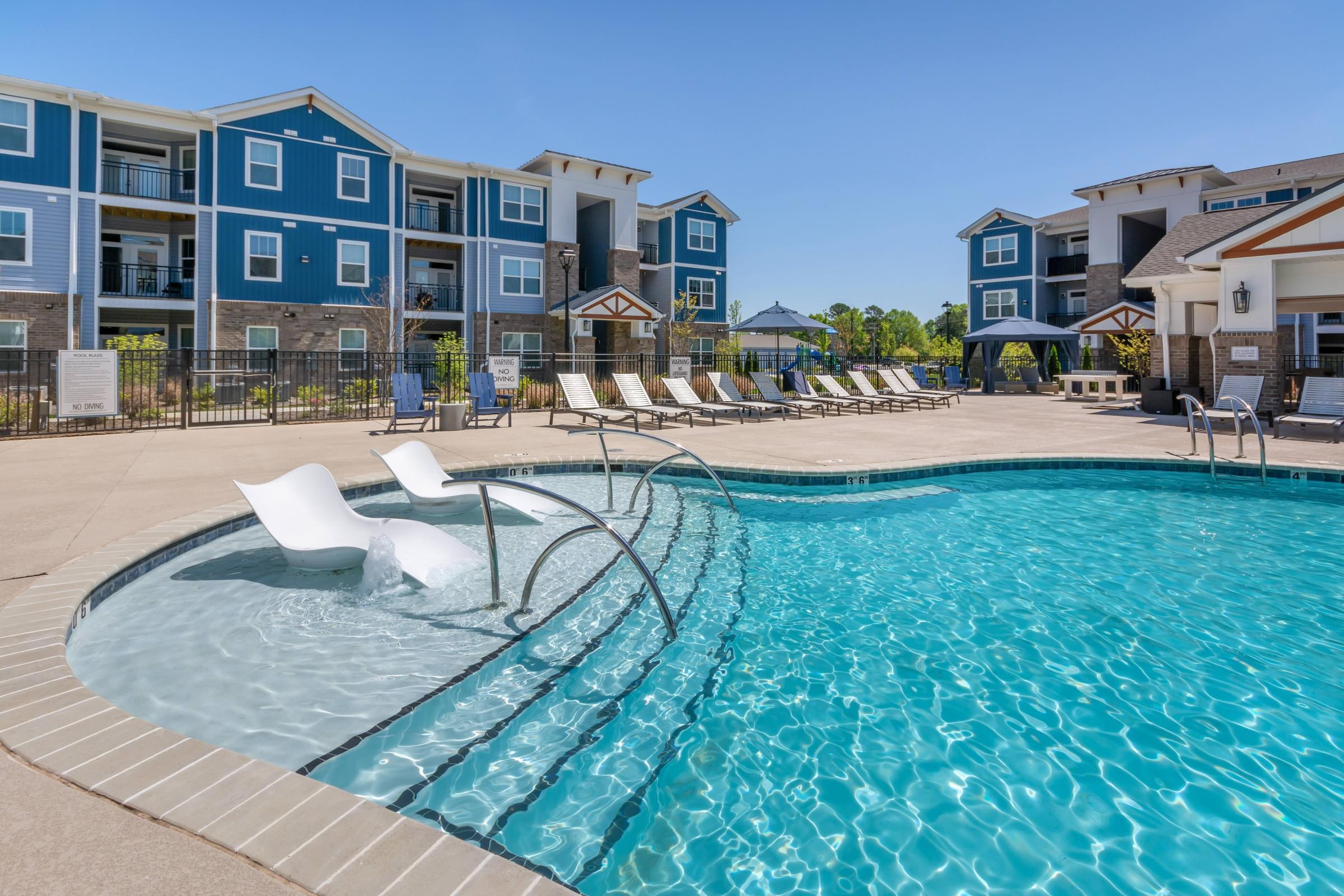 A swimming pool with lounge chairs in front of apartment buildings.