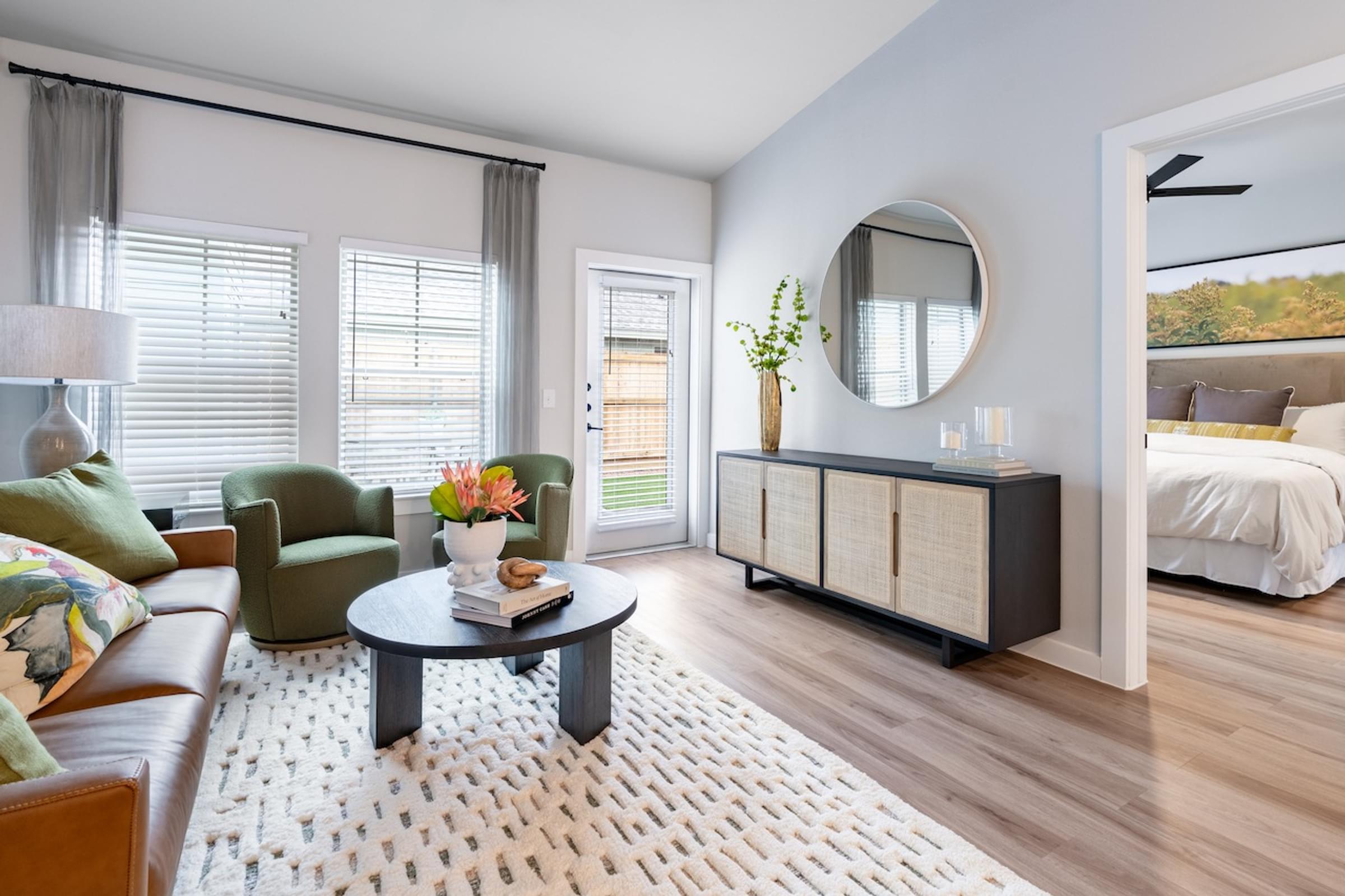 A living room with a brown leather couch, a round mirror, and a white rug.