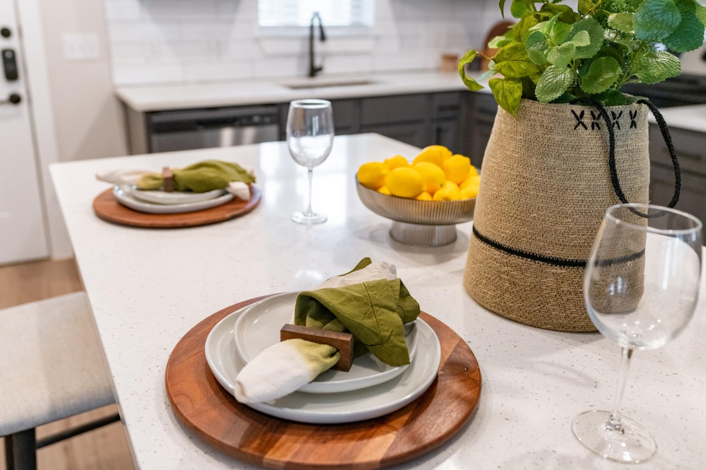 A kitchen counter with a plate of food, a glass of wine, and a potted plant.