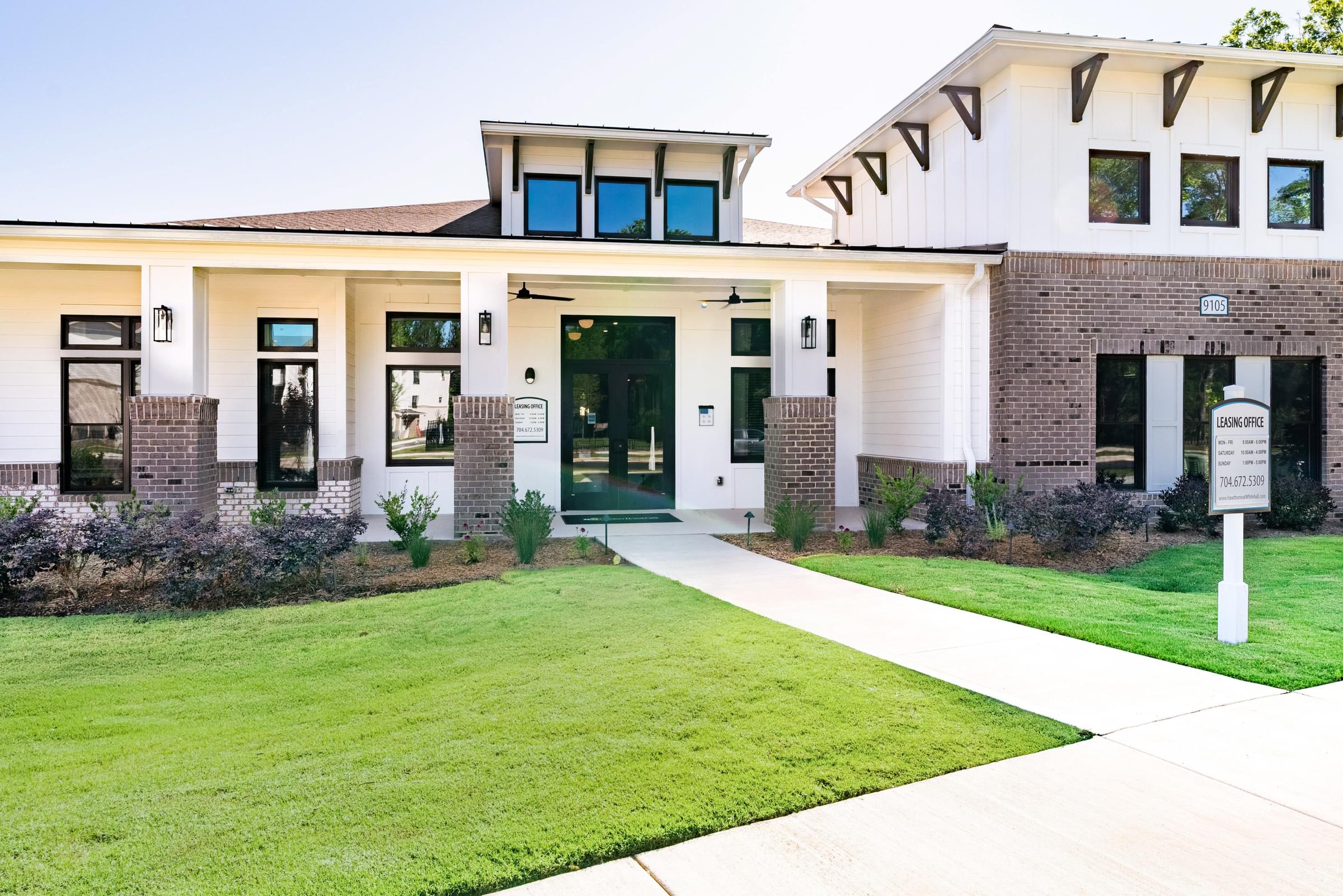 A modern building with a white and brown facade and a green lawn in front.