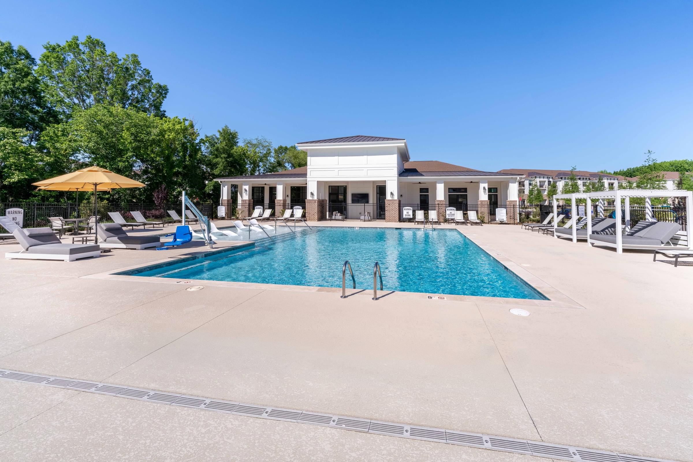 A large swimming pool in front of a house with a sun lounger.