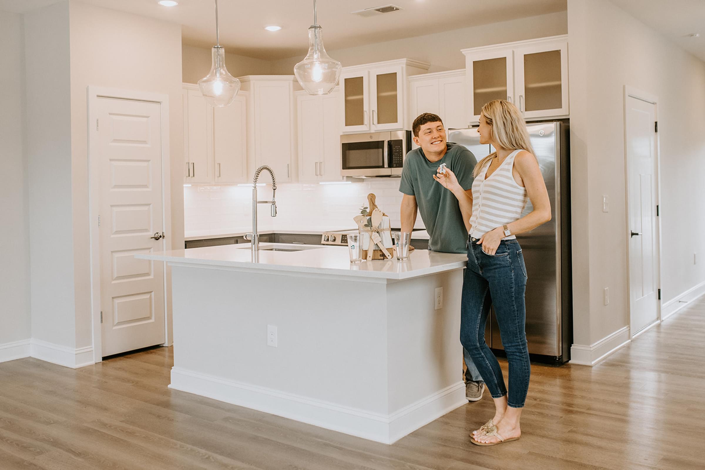A man and woman are standing in a kitchen with a sink and a refrigerator.
