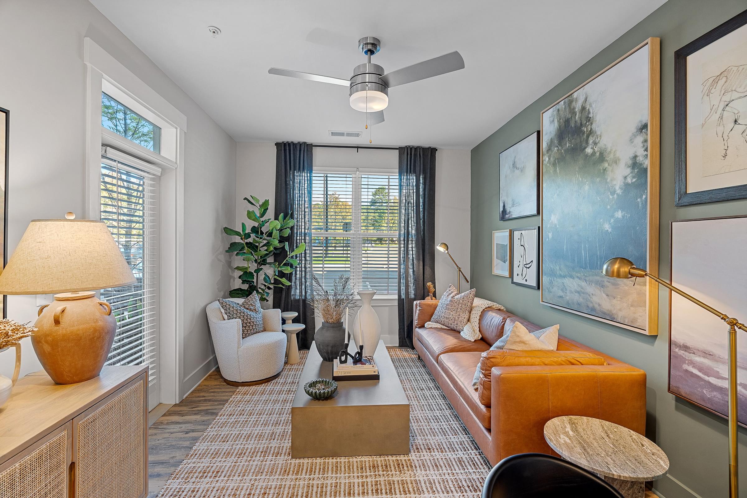 A living room with a couch, a coffee table, pictures on the wall and a ceiling fan.