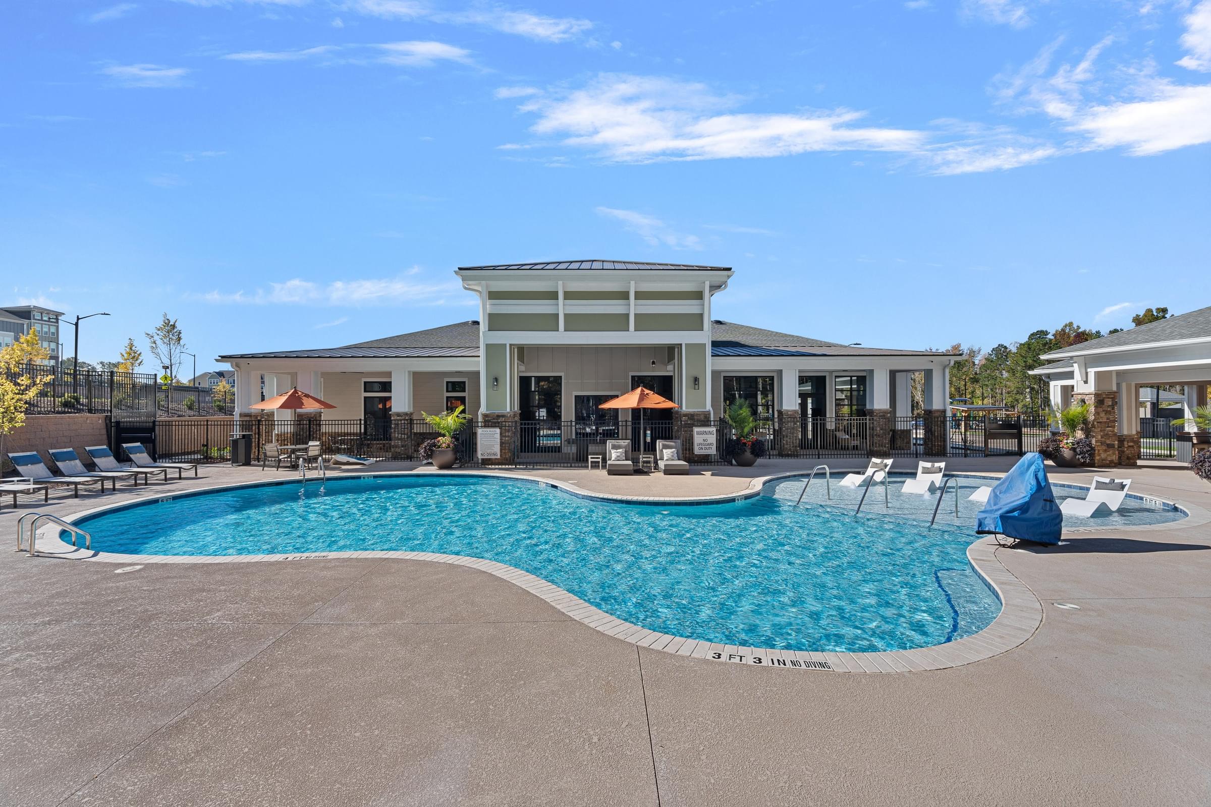 A large swimming pool with lounging chairs, umbrellas and tables surrounding.