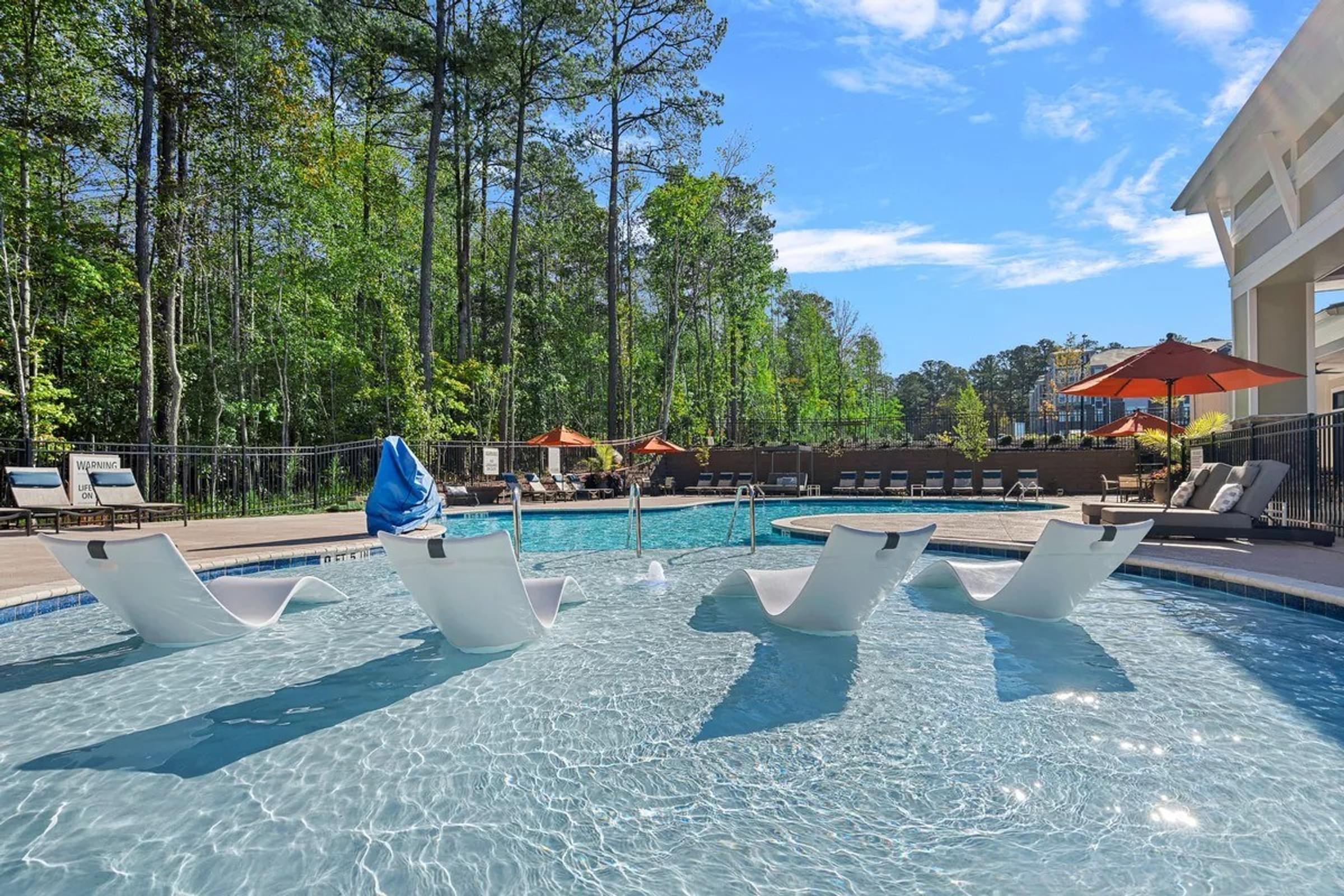 Outdoor pool with white lounger chairs and an orange umbrella.